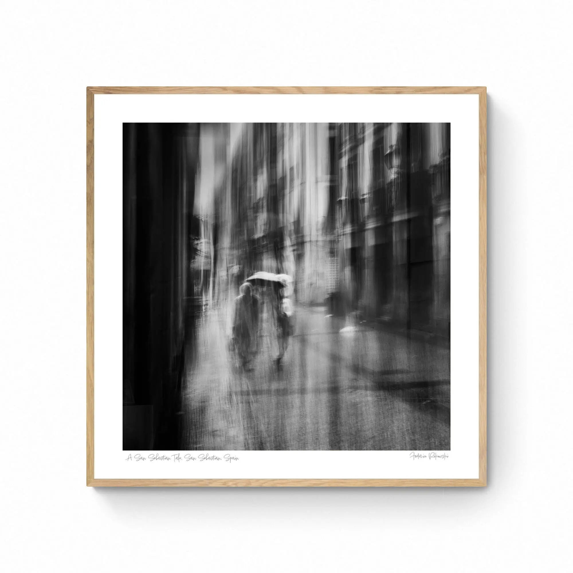 Black and white image of blurred figures under an umbrella on a rainy street in San Sebastian, Spain, creating an ethereal atmosphere.