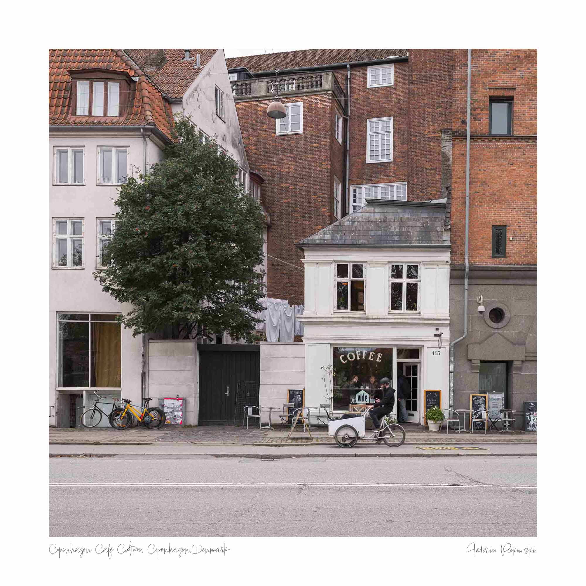 A cozy café sits nestled between classic Copenhagen buildings, with bicycles parked outside, invoking the city's relaxed urban atmosphere.