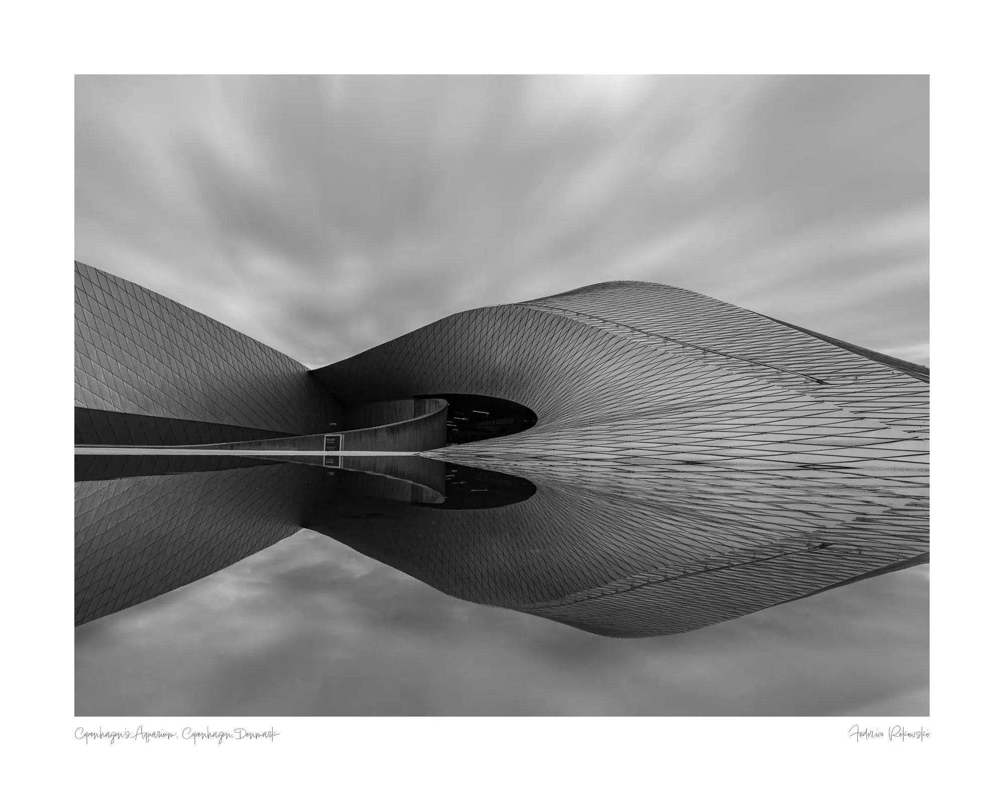 Black and white image of The Blue Planet Aquarium in Copenhagen with its reflective, wavy facade against a blurred sky.