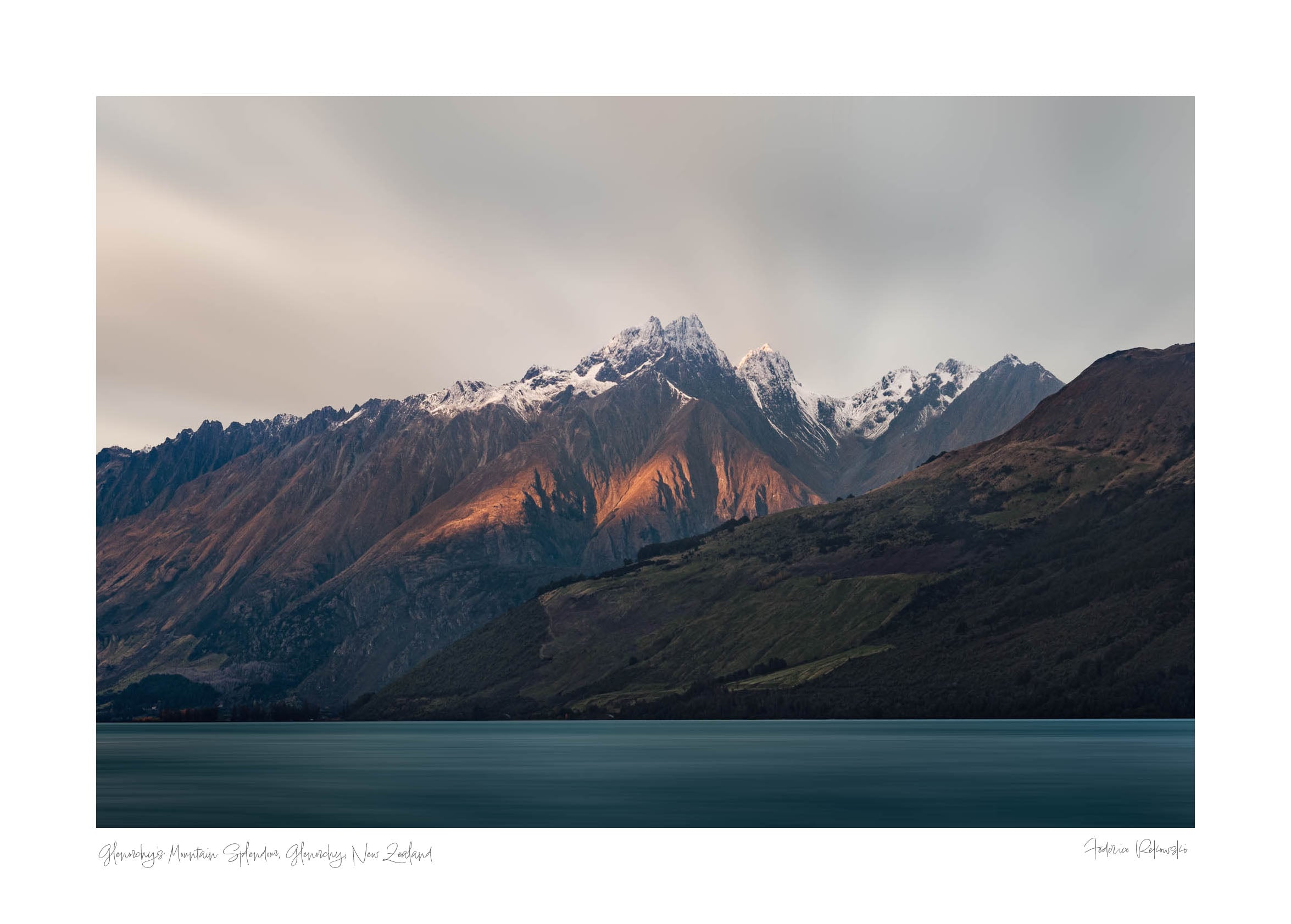 Last light of dusk casting a warm glow on the snowy peaks of mountains in Glenorchy, New Zealand, with a calm lake in the foreground.