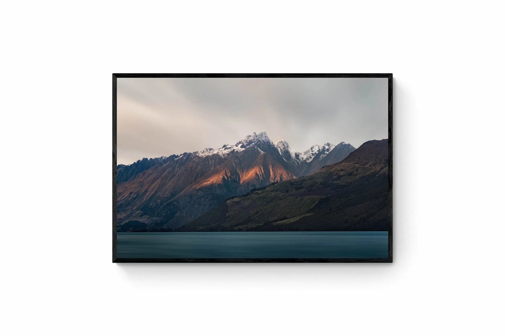 Last light of dusk casting a warm glow on the snowy peaks of mountains in Glenorchy, New Zealand, with a calm lake in the foreground.