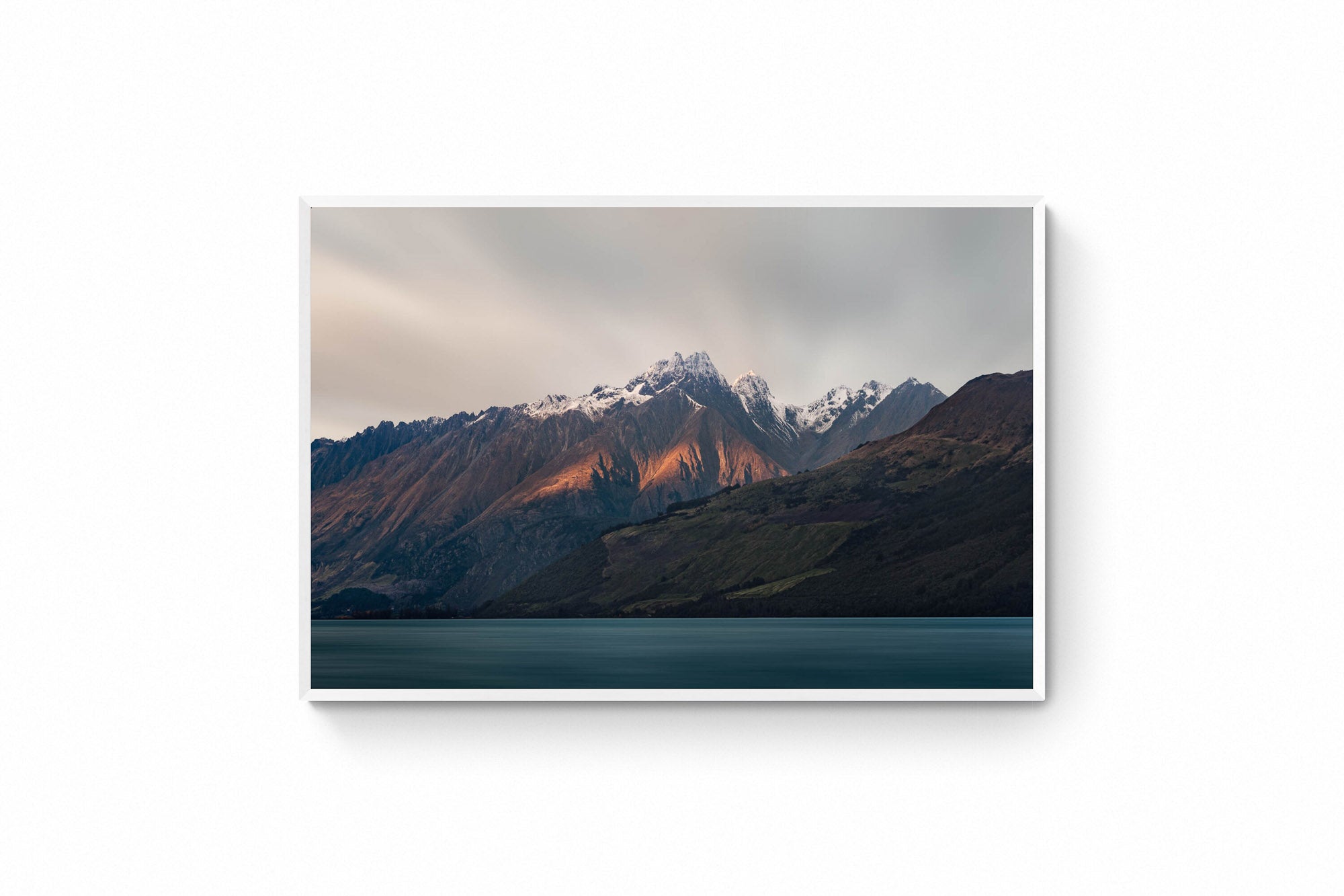 Last light of dusk casting a warm glow on the snowy peaks of mountains in Glenorchy, New Zealand, with a calm lake in the foreground.