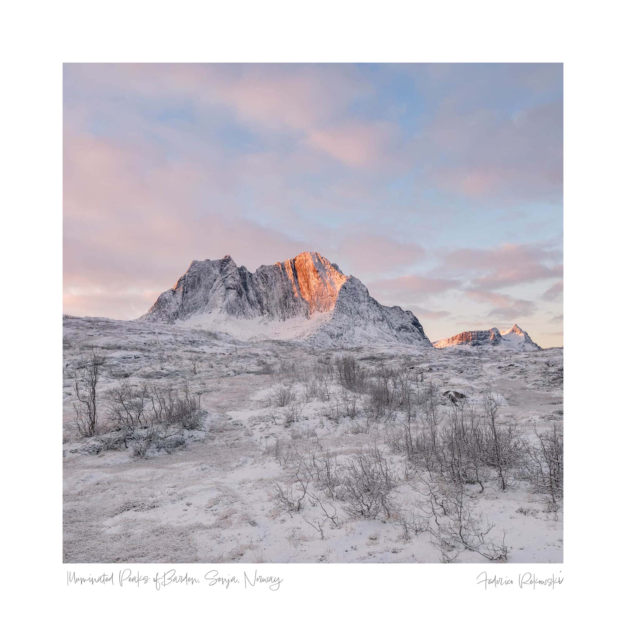 First light of dawn illuminating the snowy peaks at the entry of Barden trail in Lofoten with a soft pink sky.