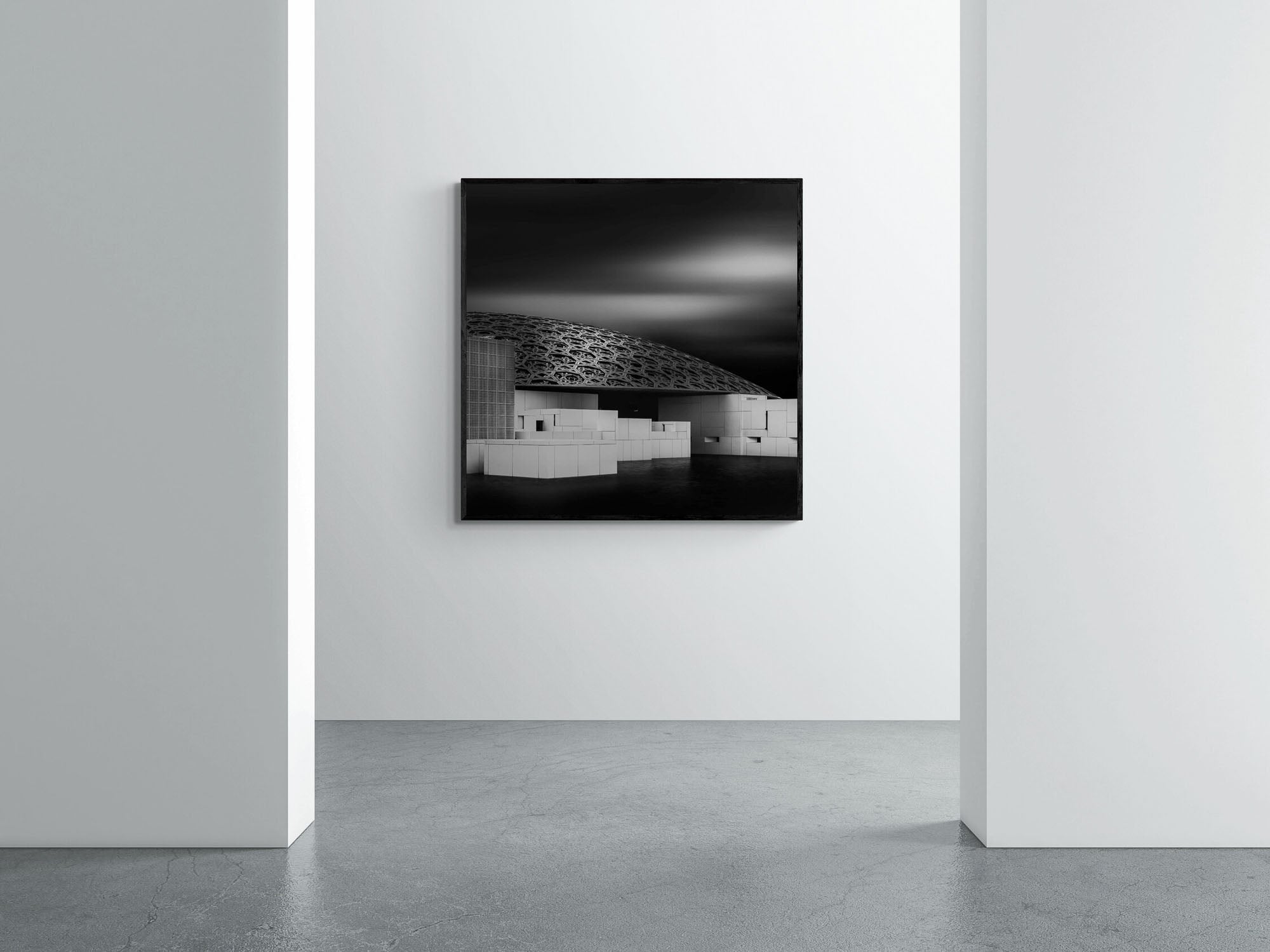 Black and white photo of the Louvre Abu Dhabi, highlighting the intricate geometric patterns of the dome against a dramatic sky.