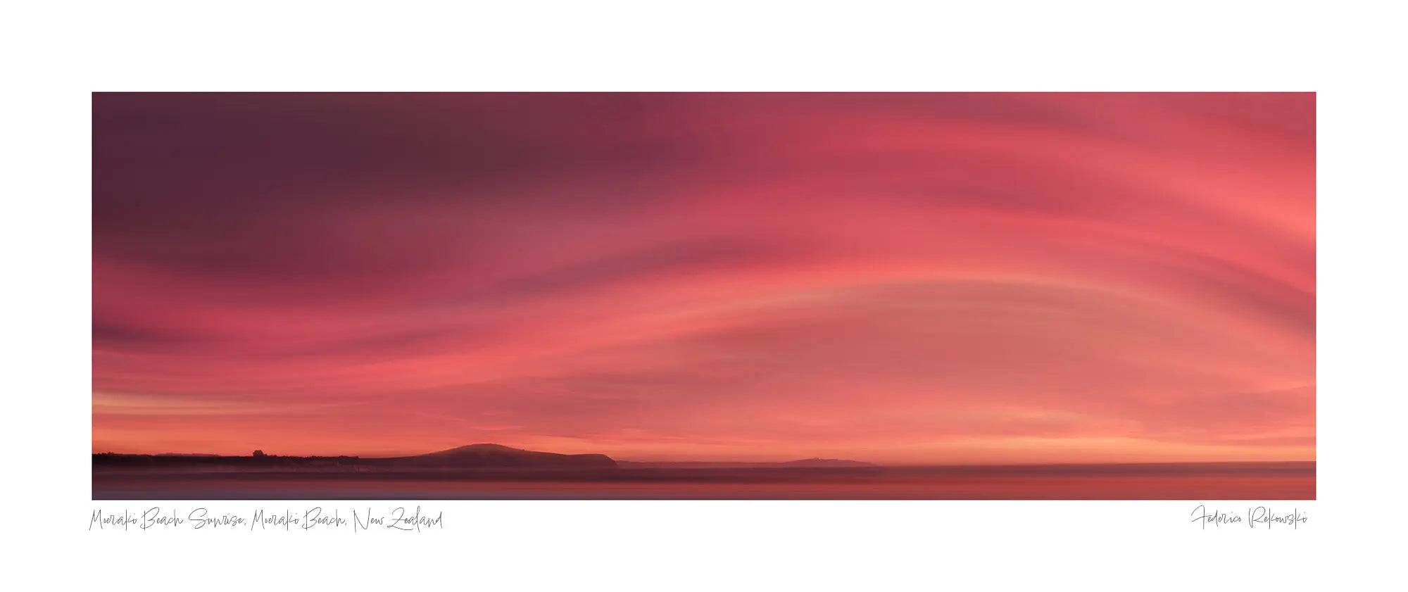 Sunrise over Moeraki Beach depicted in a photograph, showcasing vibrant red and pink clouds stretched across the sky.