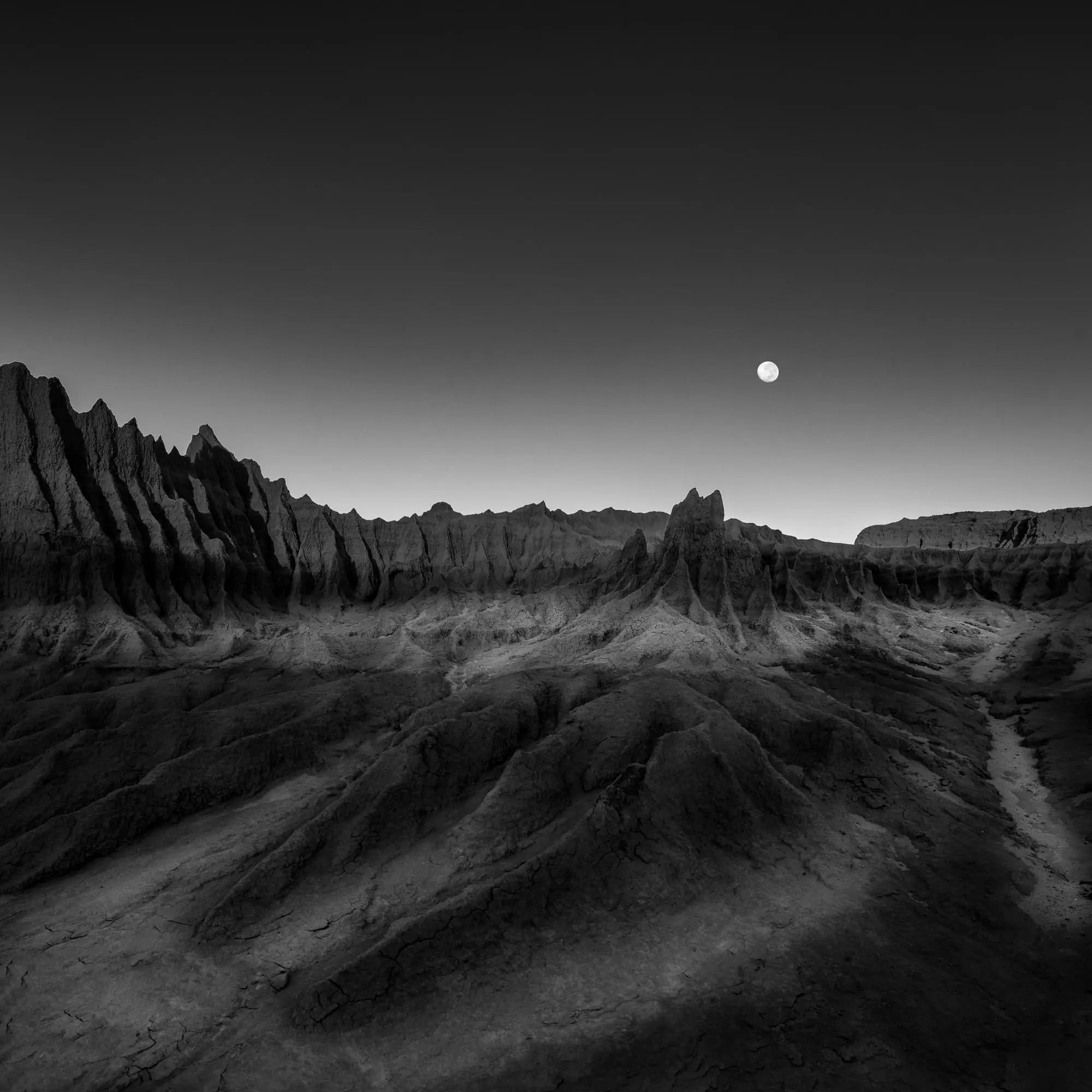 Black and white photo titled "Moonrise Over Mungo," depicting the moon rising above the dramatic landscapes of Mungo National Park, Australia.