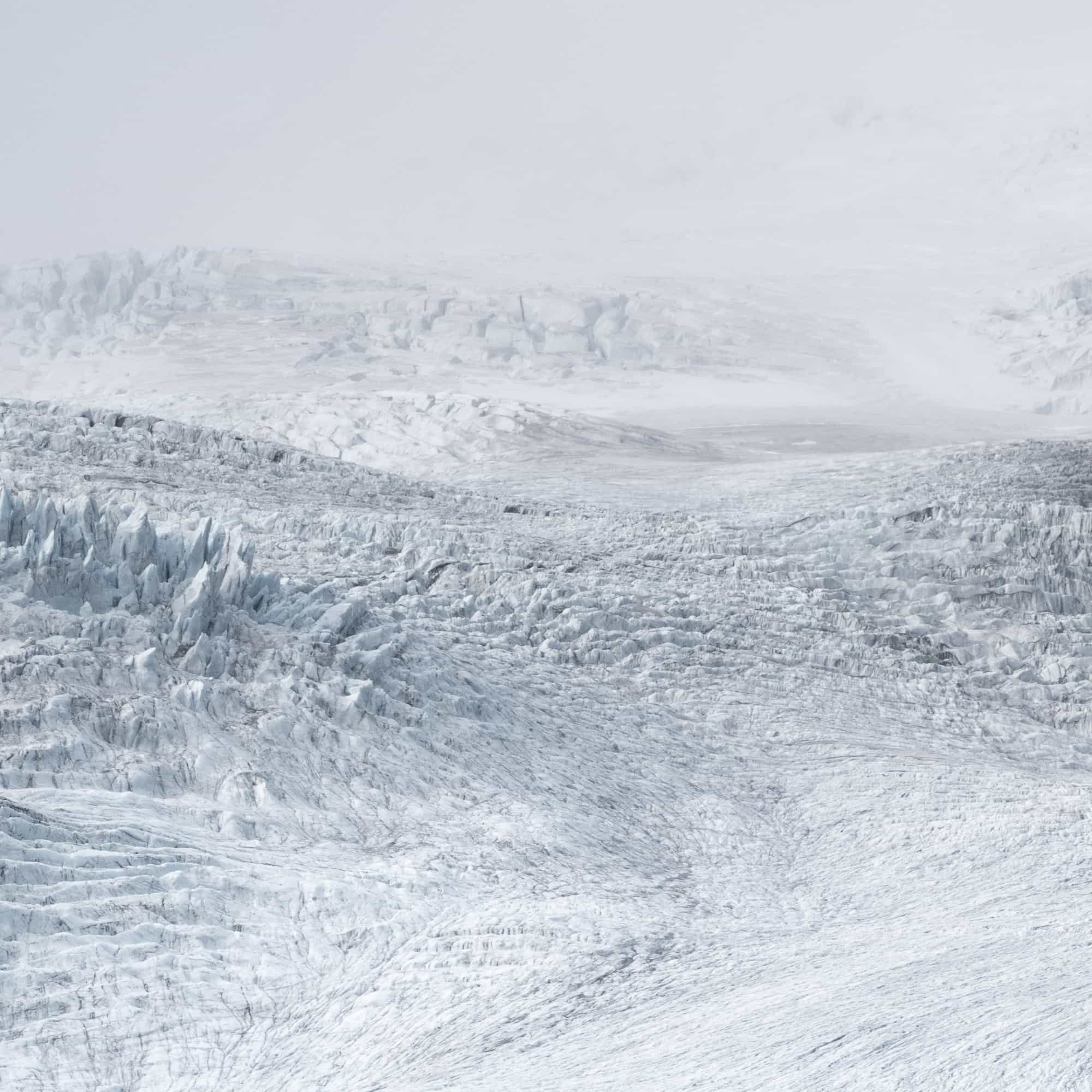 A monochromatic view of an expansive glacier in Iceland, showing textured ice formations under a subtle gray sky.