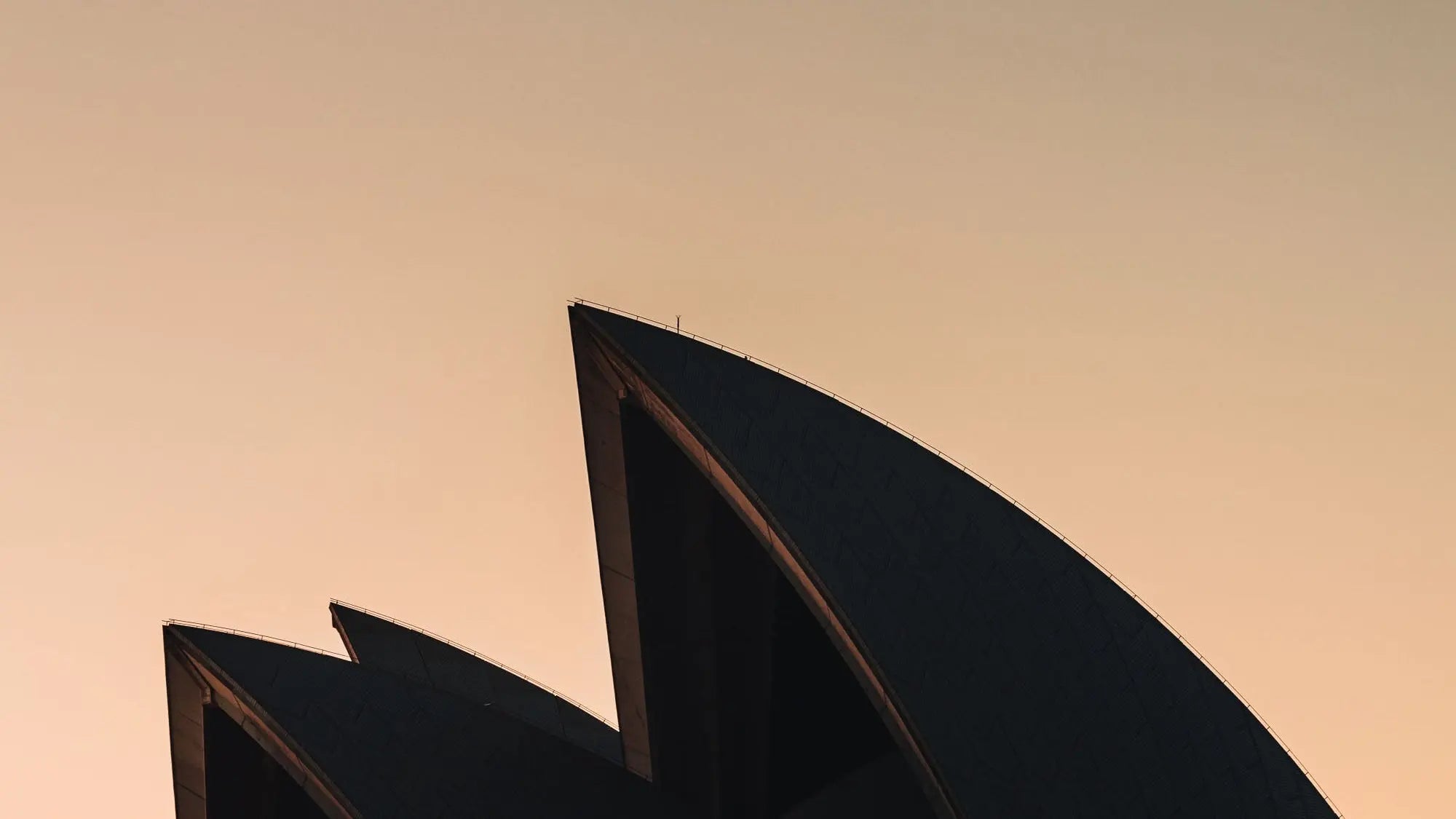 The iconic sails of the Sydney Opera House in silhouette against the warm tones of sunrise.