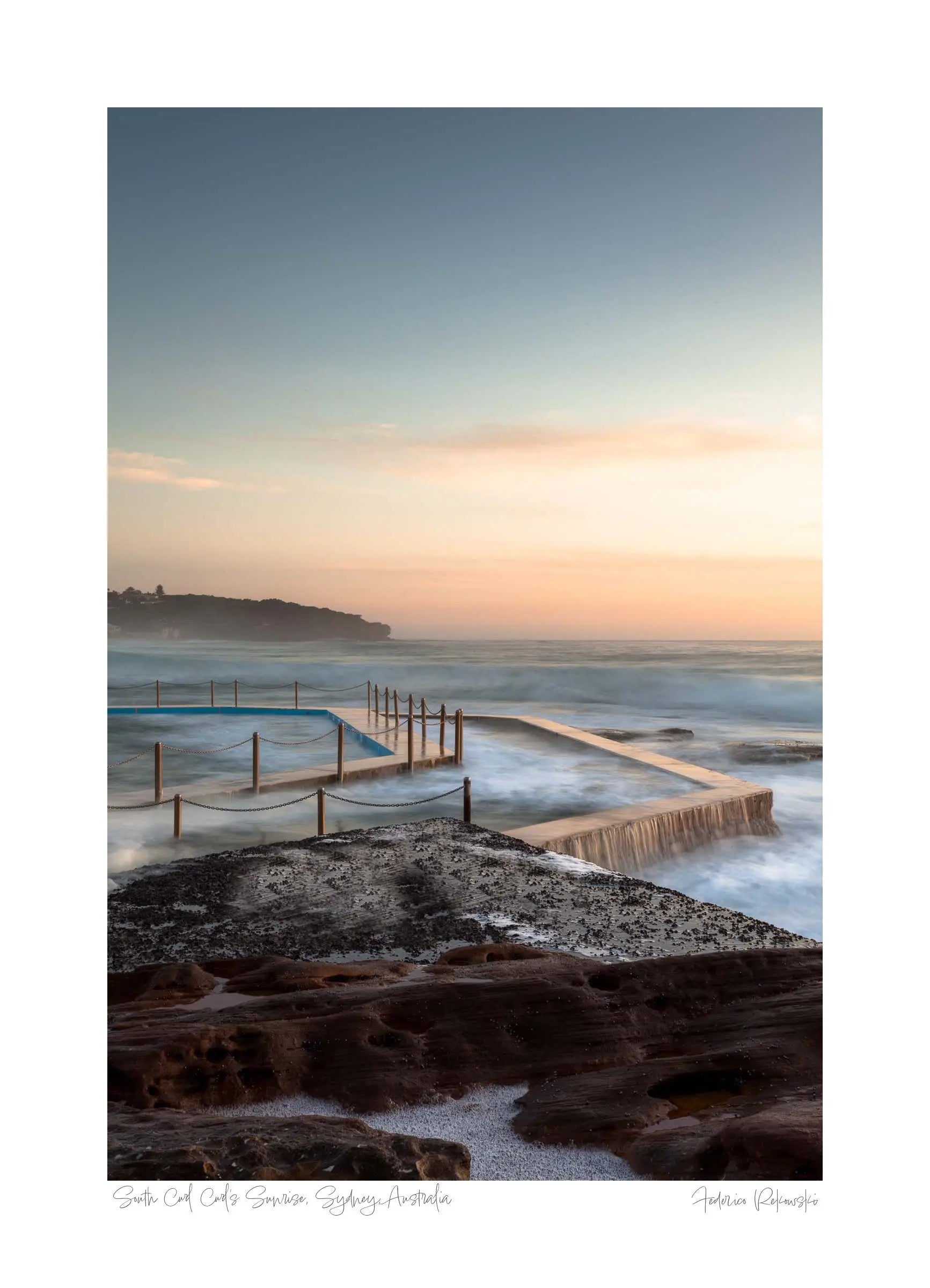 Twilight at South Curl Curl pool with smooth water flowing over its edges, bordered by textured rocks against a pastel sky.