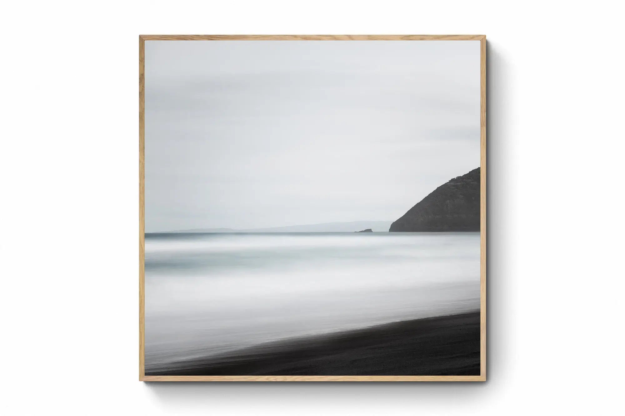 A minimalist long exposure photo of the calm sea meeting the dark sands of St. Clair's Beach in New Zealand, with a headland silhouette on the right.