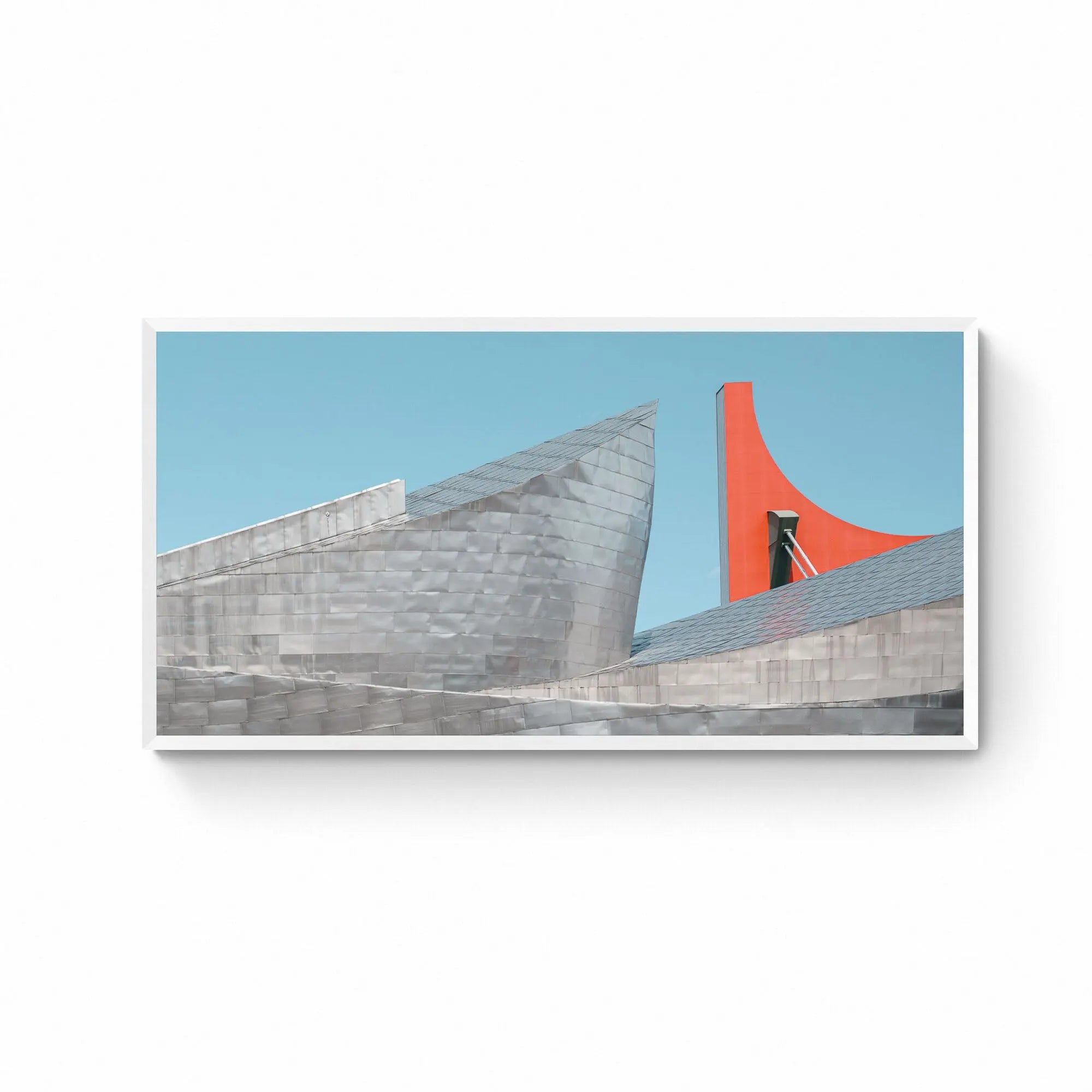 The Guggenheim Museum Bilbao, with its metallic curves contrasted by a bright red architectural feature against a clear blue sky.