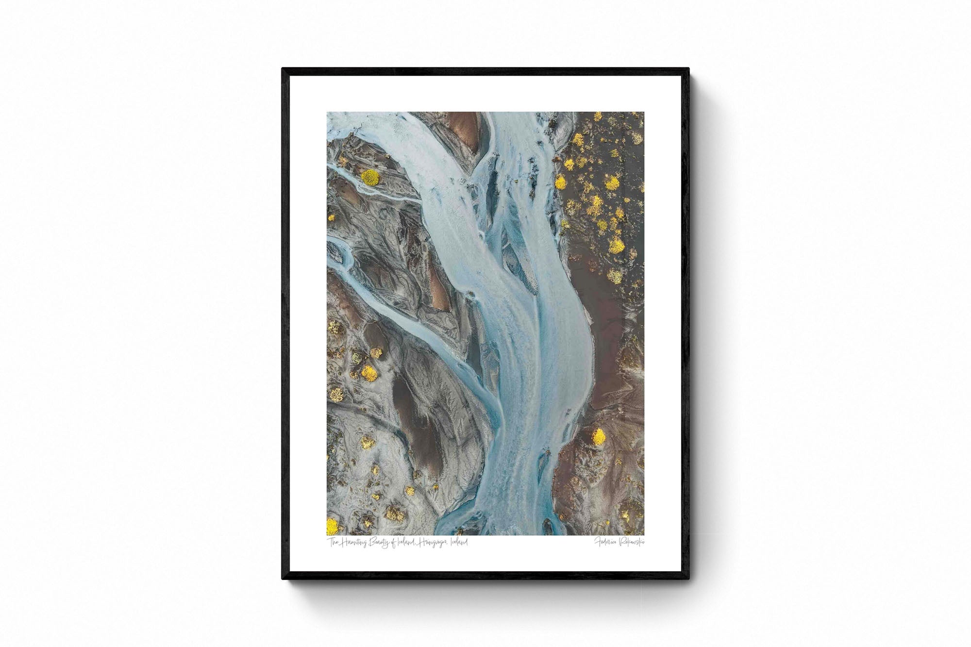 Aerial photo of a ghostly pale blue river snaking through the darker earth in Iceland, with patches of bright yellow flora.