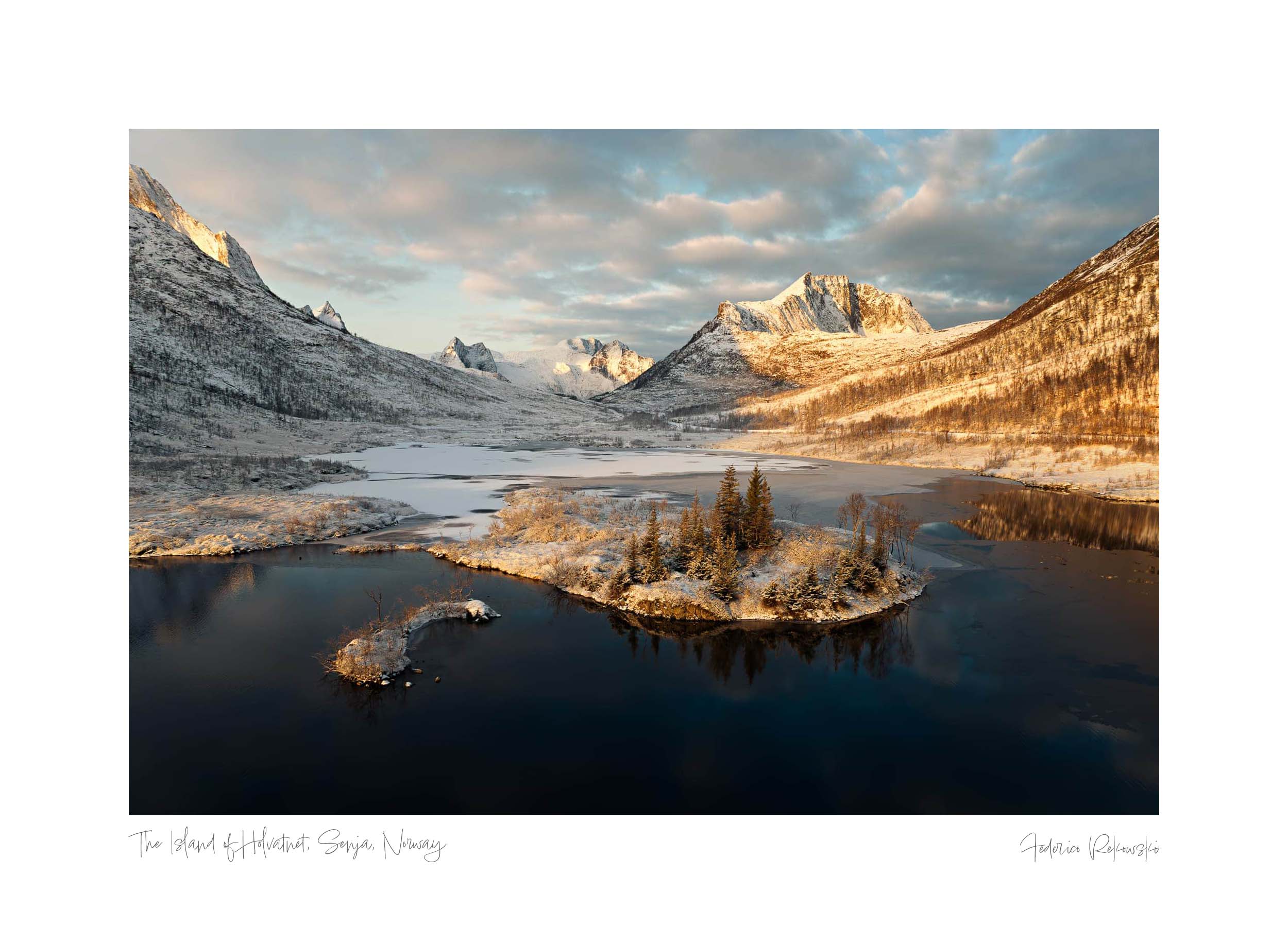 Sunset illuminating the snowy peaks and frozen lake of Holvatnet in Senja, Norway, with frosted trees on an islet.
