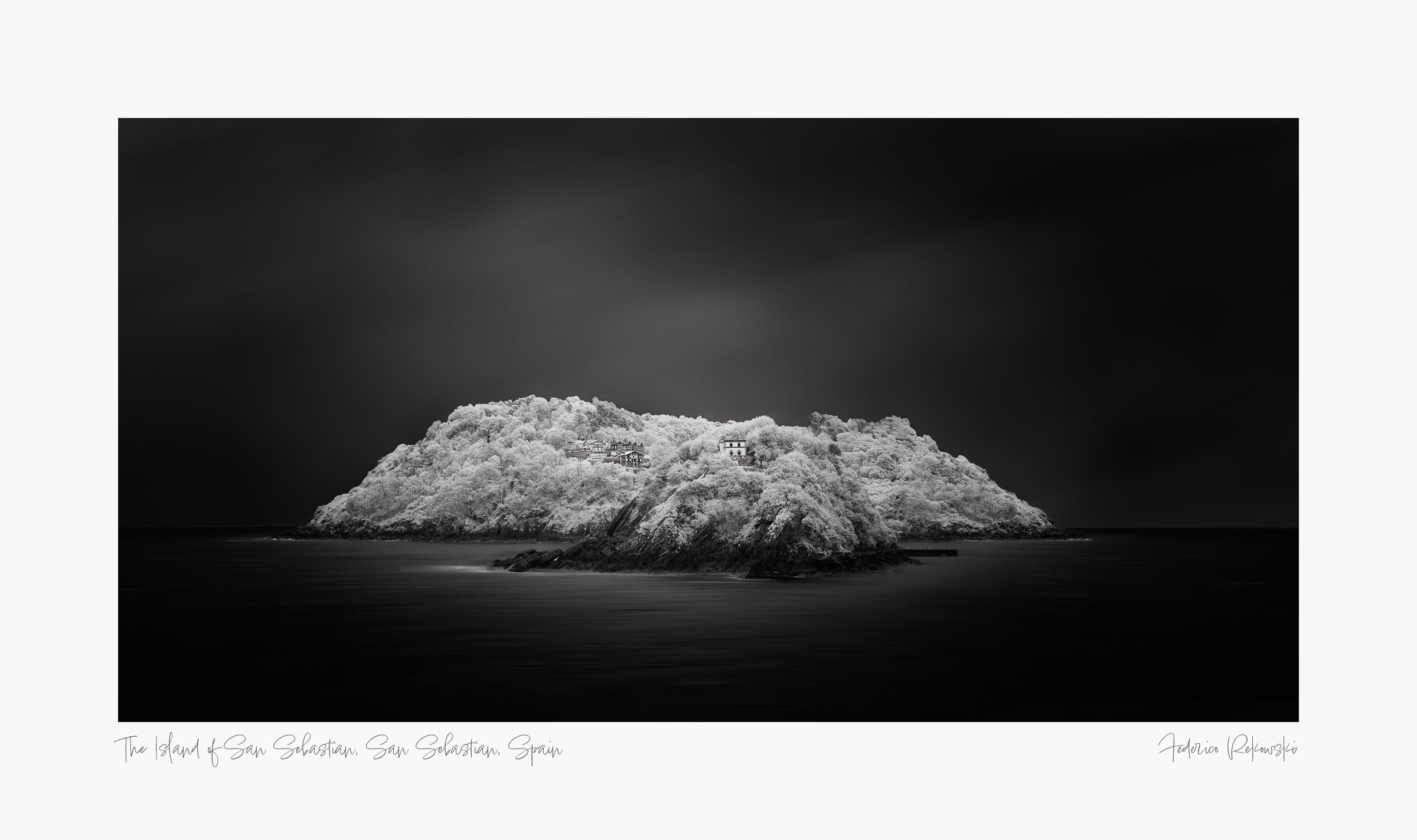 "Black and white image of an isolated island in San Sebastian, Spain, with radiant white foliage under a dark sky."