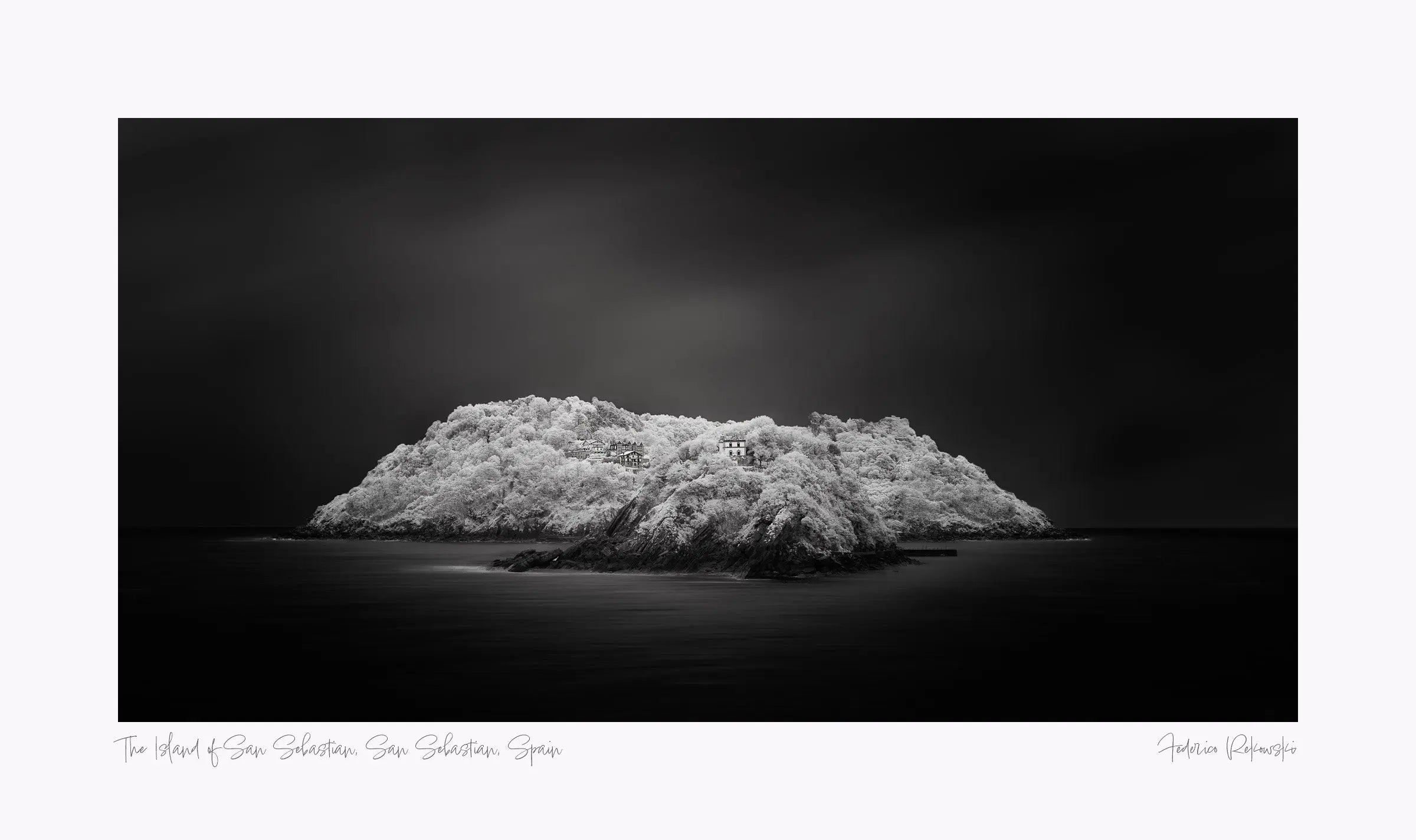"Black and white image of an isolated island in San Sebastian, Spain, with radiant white foliage under a dark sky."