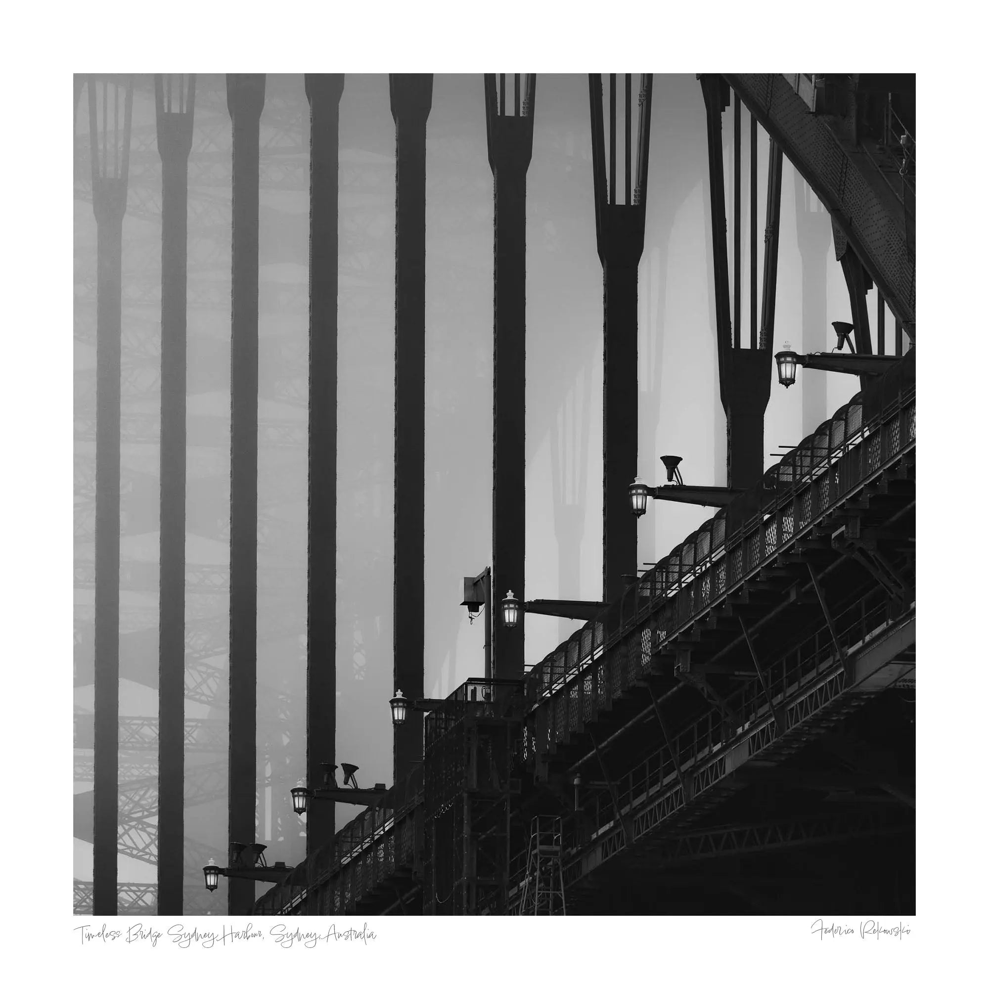 Monochrome image of Sydney Harbour Bridge, showing the contrast of the stark, strong lines of its arches and street lamps against the light sky.