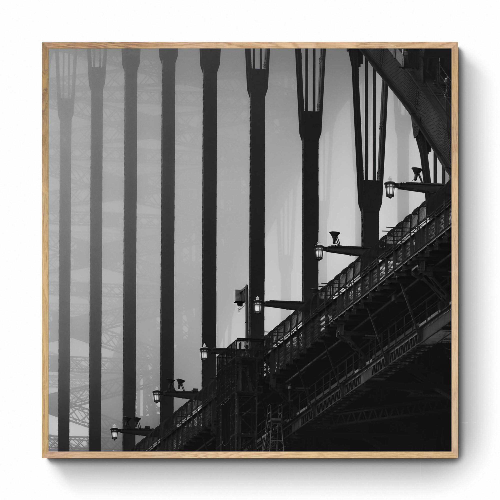 Monochrome image of Sydney Harbour Bridge, showing the contrast of the stark, strong lines of its arches and street lamps against the light sky.