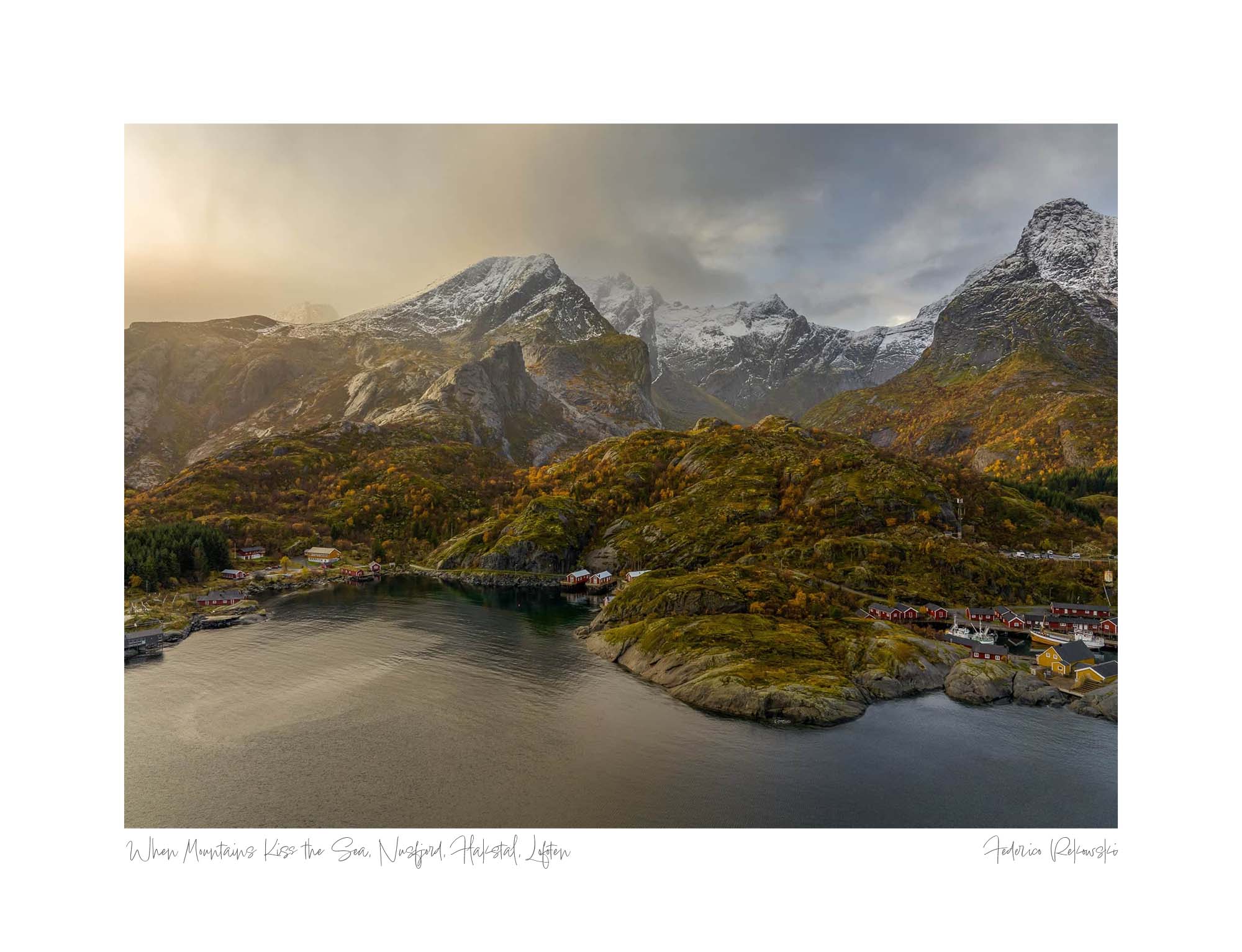 Aerial view of a fjord in Lofoten, Norway, during autumn with snow-capped mountains and colorful houses nestled amongst golden-hued trees.