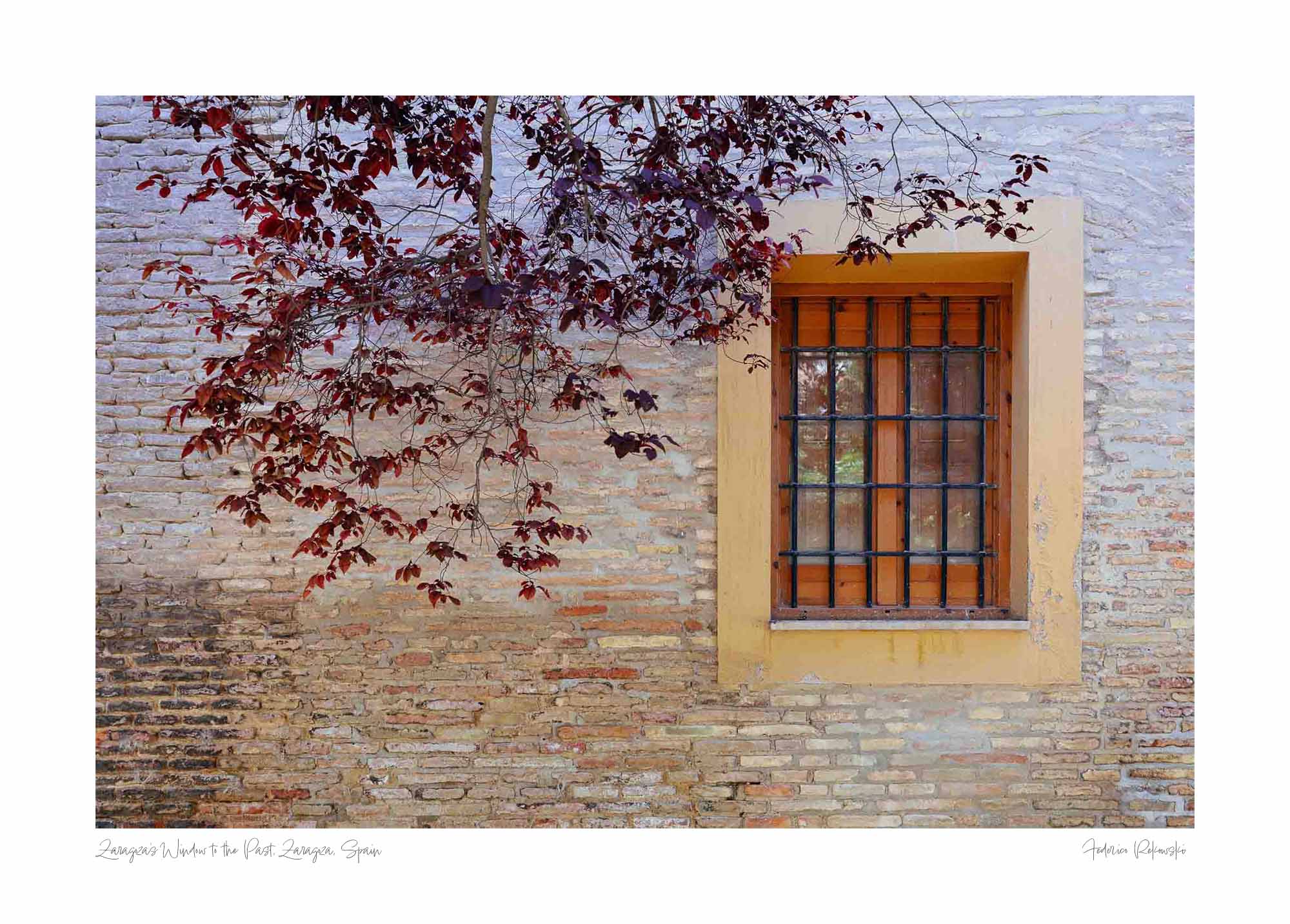 A rustic window with a yellow frame set in an old brick wall, adorned by autumn leaves, in Zaragoza, Spain.
