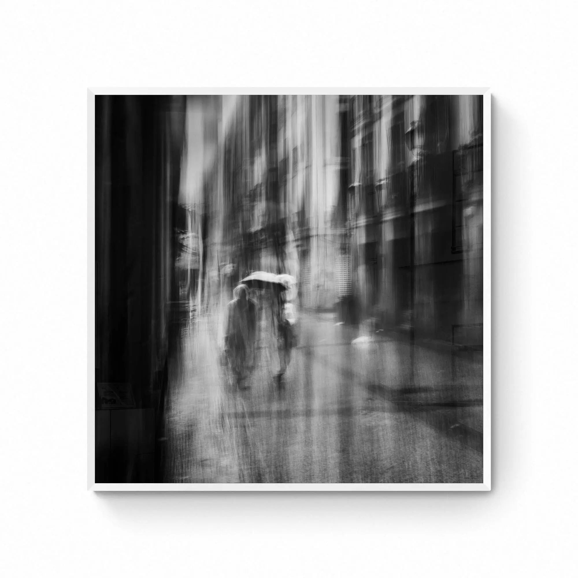 Black and white image of blurred figures under an umbrella on a rainy street in San Sebastian, Spain, creating an ethereal atmosphere.