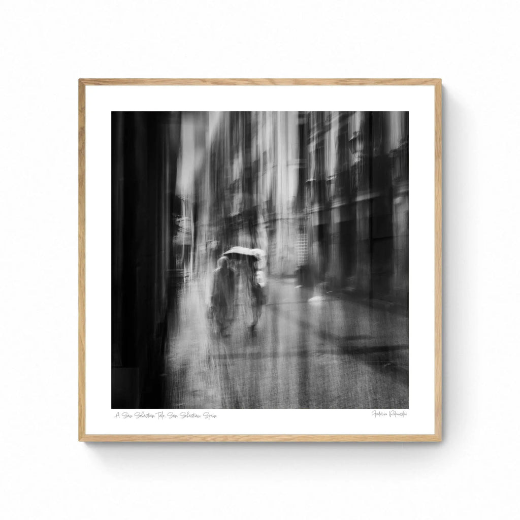 Black and white image of blurred figures under an umbrella on a rainy street in San Sebastian, Spain, creating an ethereal atmosphere.