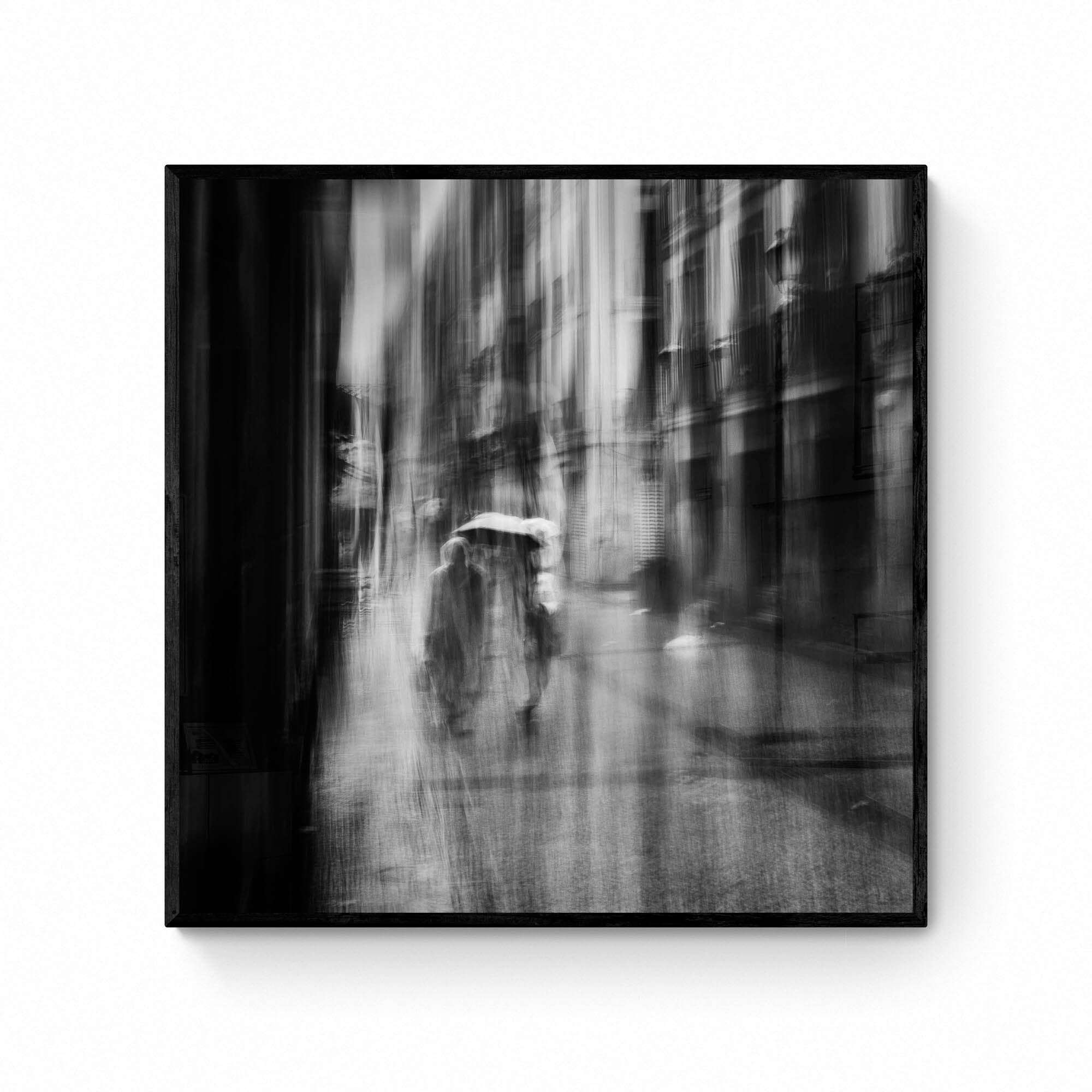 Black and white image of blurred figures under an umbrella on a rainy street in San Sebastian, Spain, creating an ethereal atmosphere.