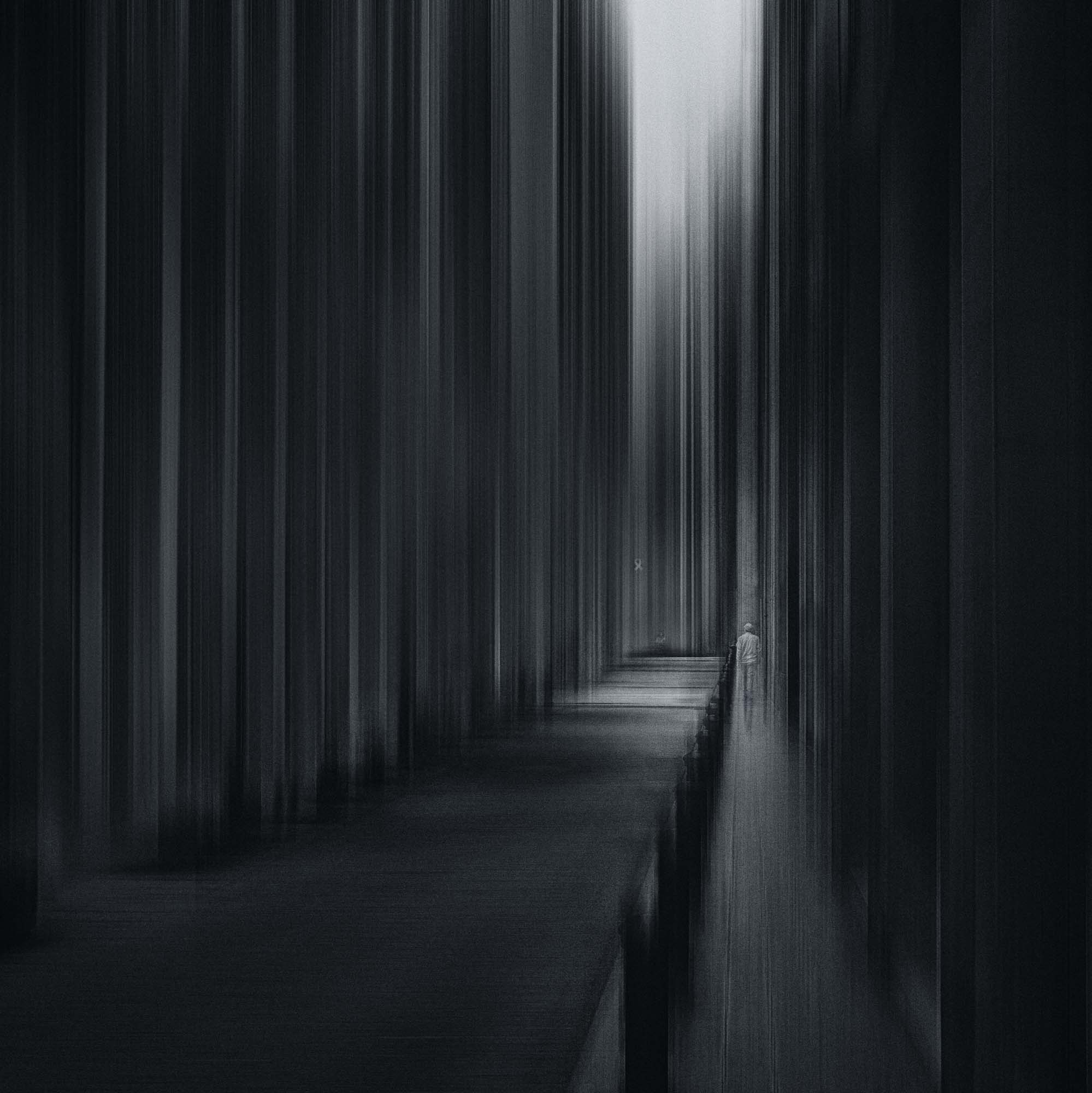 "Black and white artistic photograph showing a blurred figure walking along a path lined with vertical streaks in Barcelona."