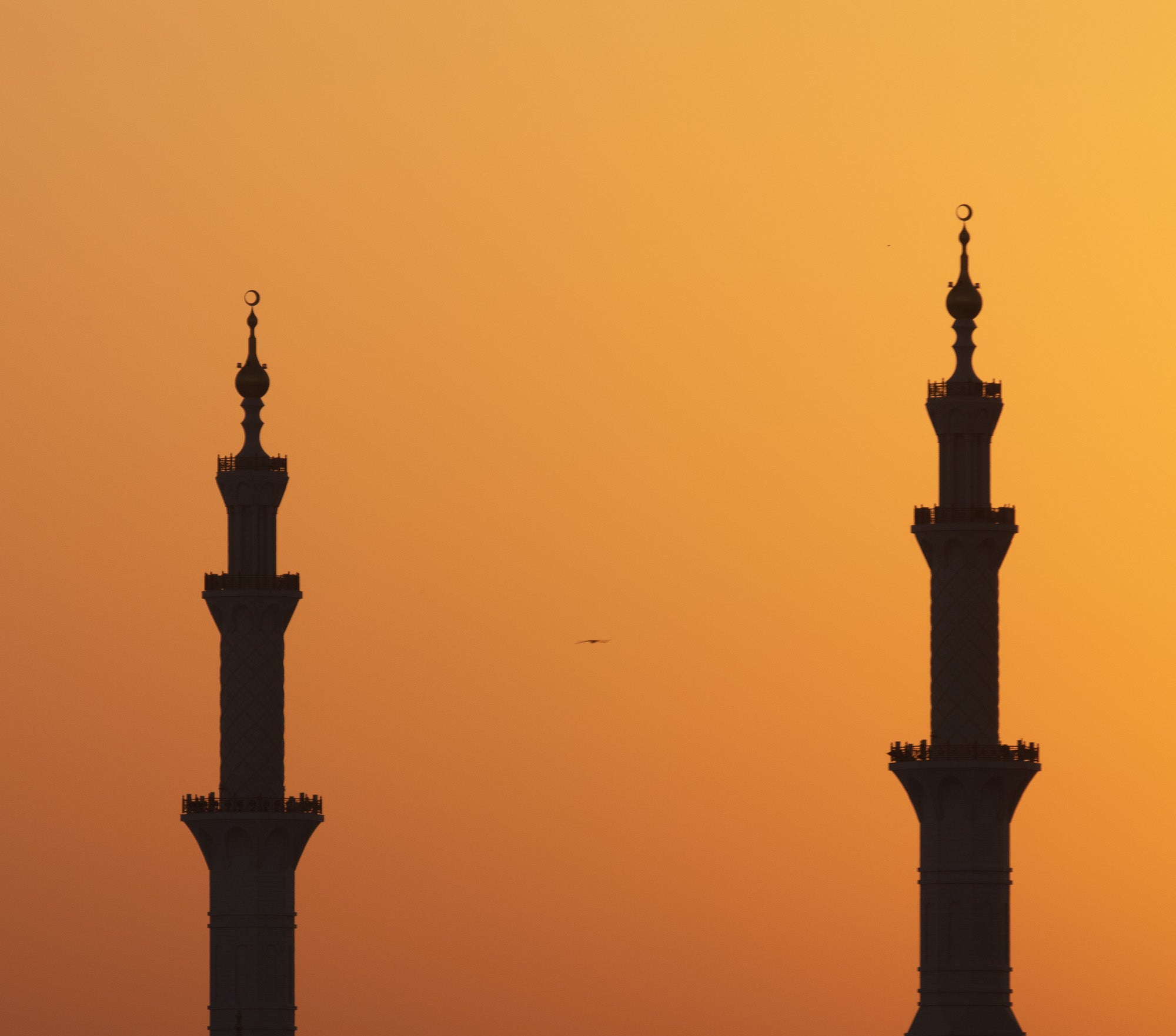 Silhouettes of two minarets against an orange sunset sky in Abu Dhabi.