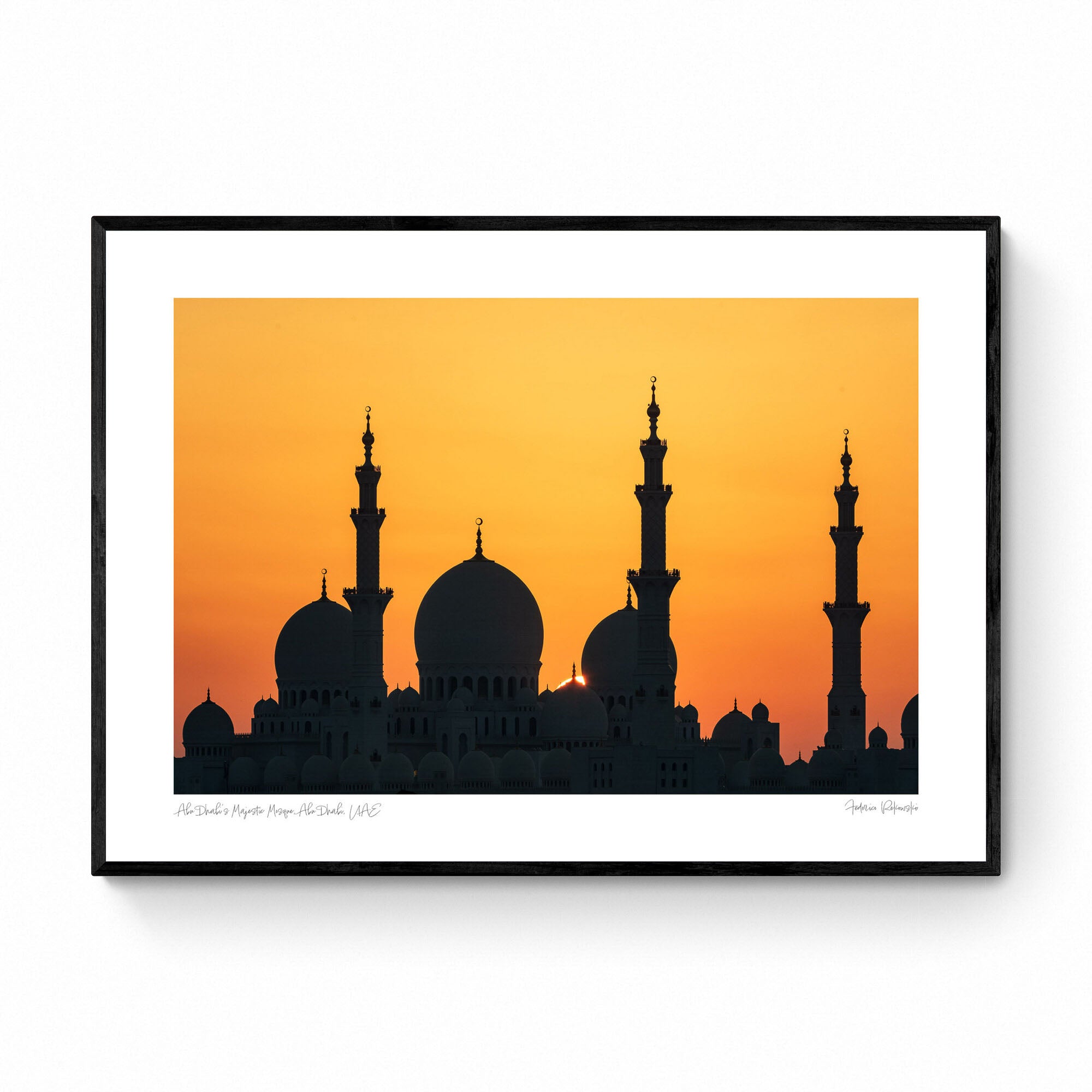 Silhouette of a grand mosque with multiple domes and minarets against a bright orange sunset sky in Abu Dhabi.