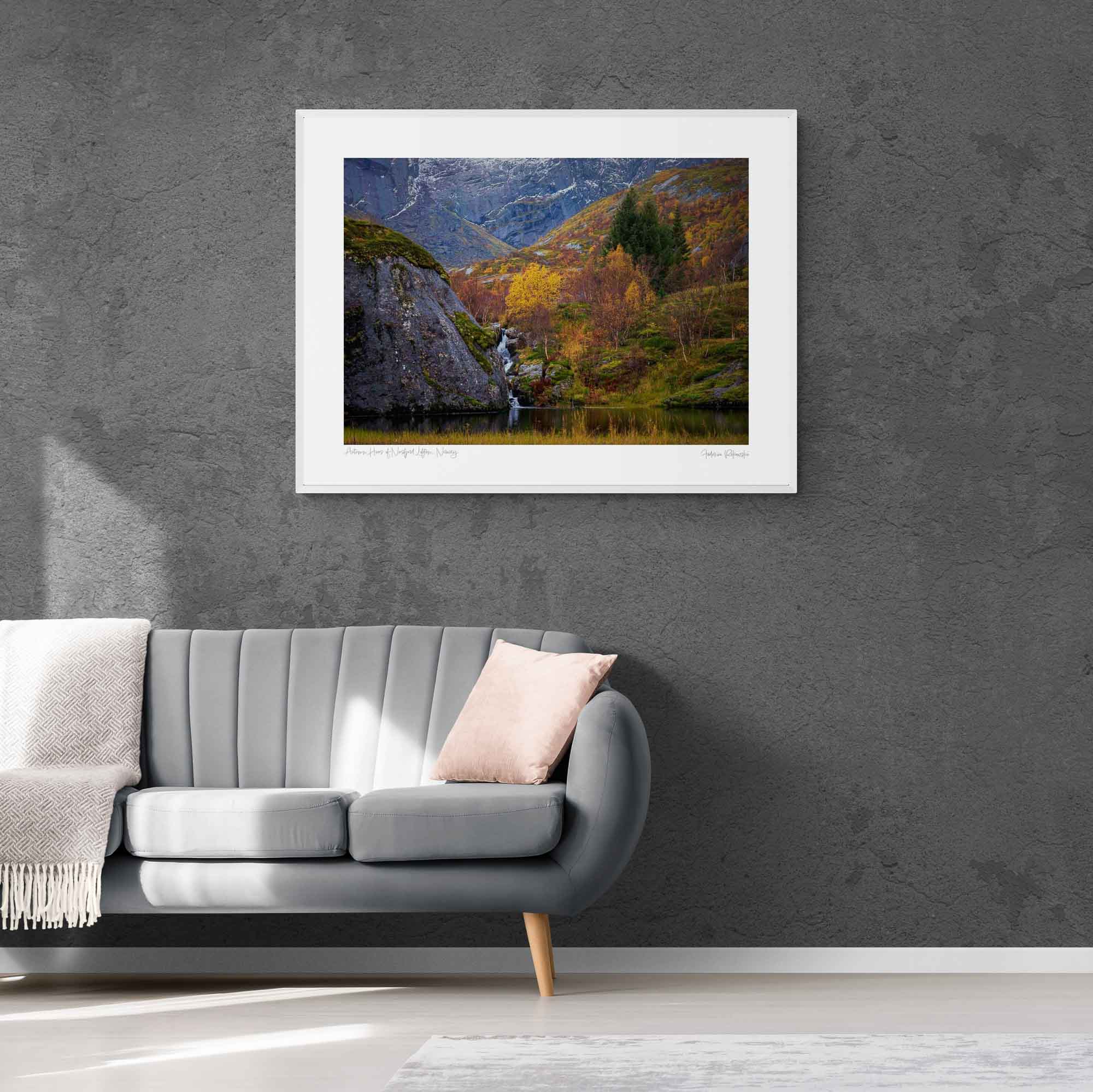 Small waterfall flowing into a pond amidst colorful autumn trees in Nusfjord, Lofoten, with rugged cliffs in the background.