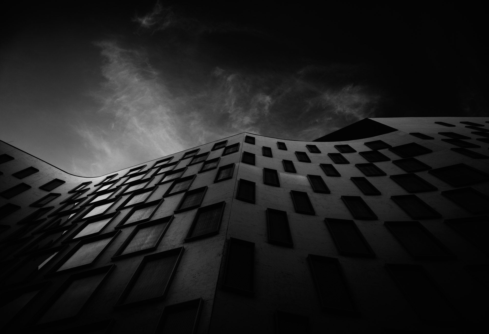 Silhouetted against the sky, the curved facade of the Vicki Sara Building at UTS, adorned with a pattern of dark windows.