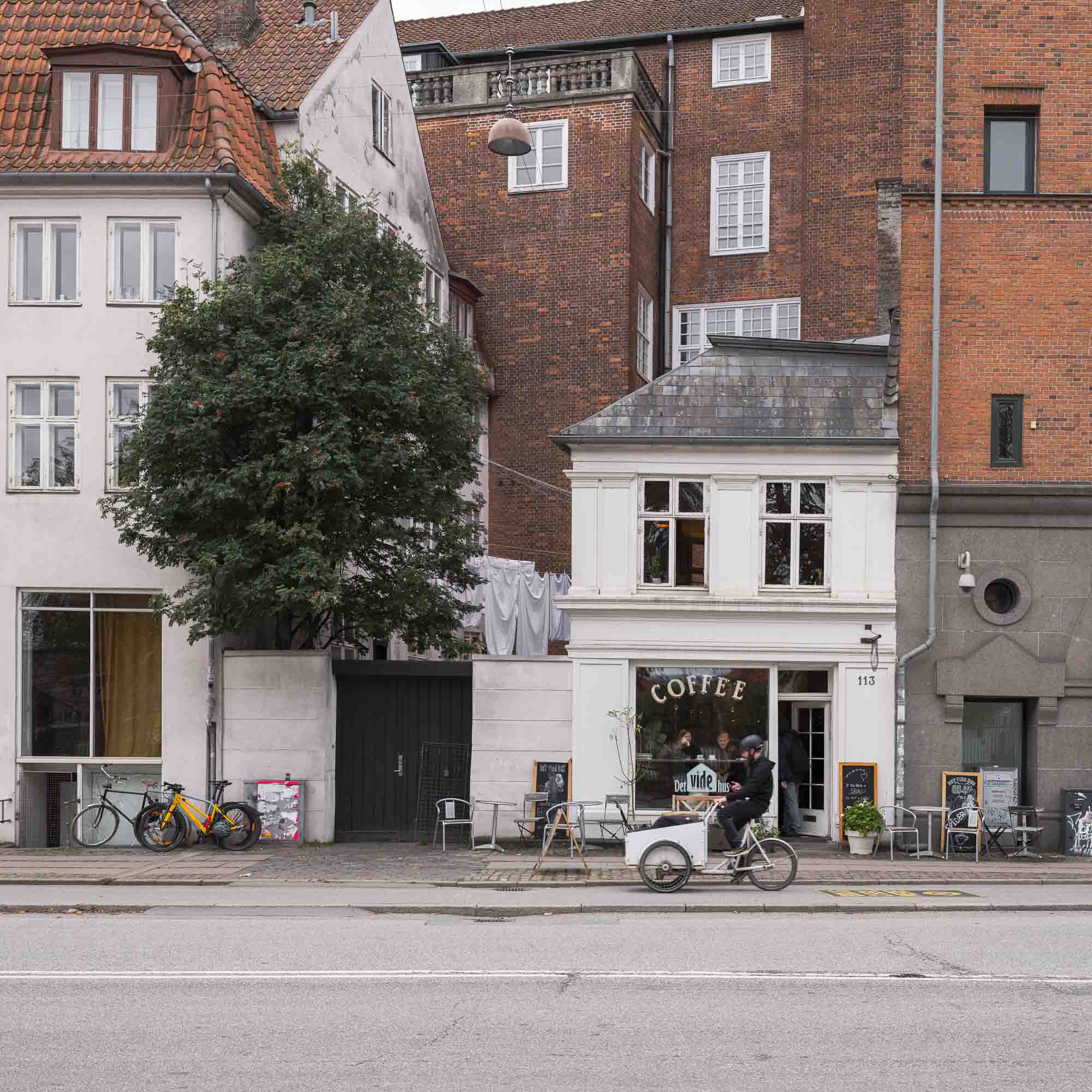 A cozy café sits nestled between classic Copenhagen buildings, with bicycles parked outside, invoking the city's relaxed urban atmosphere.