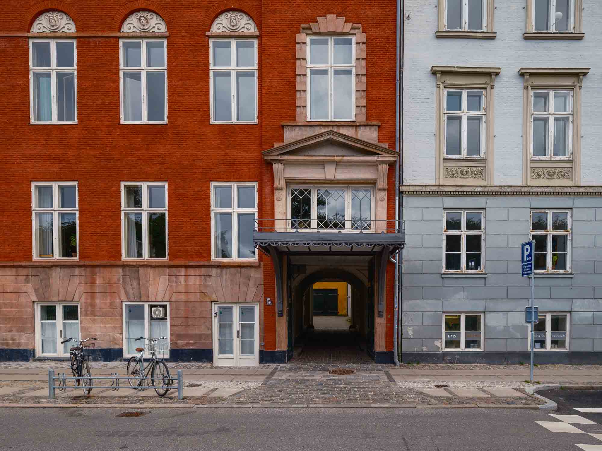 Colorful buildings in Copenhagen with a distinct red facade adjacent to a blue one, featuring a central archway leading to a hidden courtyard.