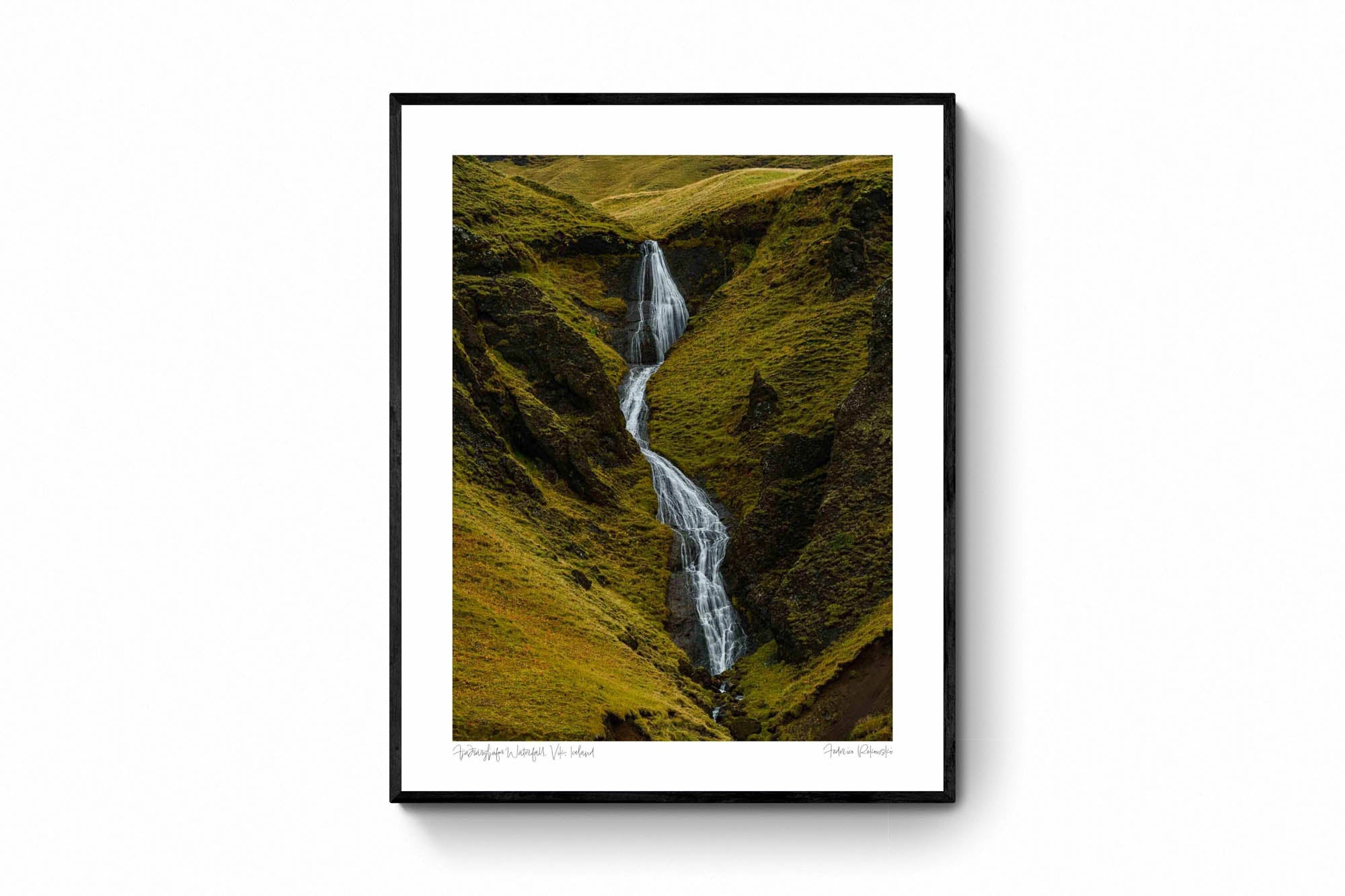 A hidden waterfall flows through the green, mossy cliffs of Fjaðrárgljúfur canyon in Iceland.