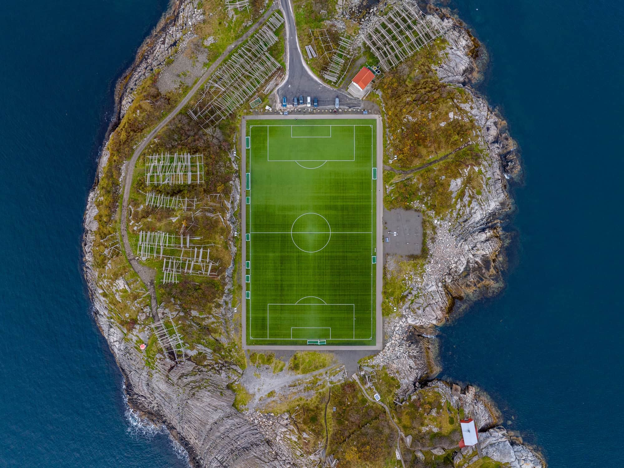 Aerial view of Henningsvær Stadium in Lofoten, Norway, with a soccer field surrounded by rocky terrain and sea.