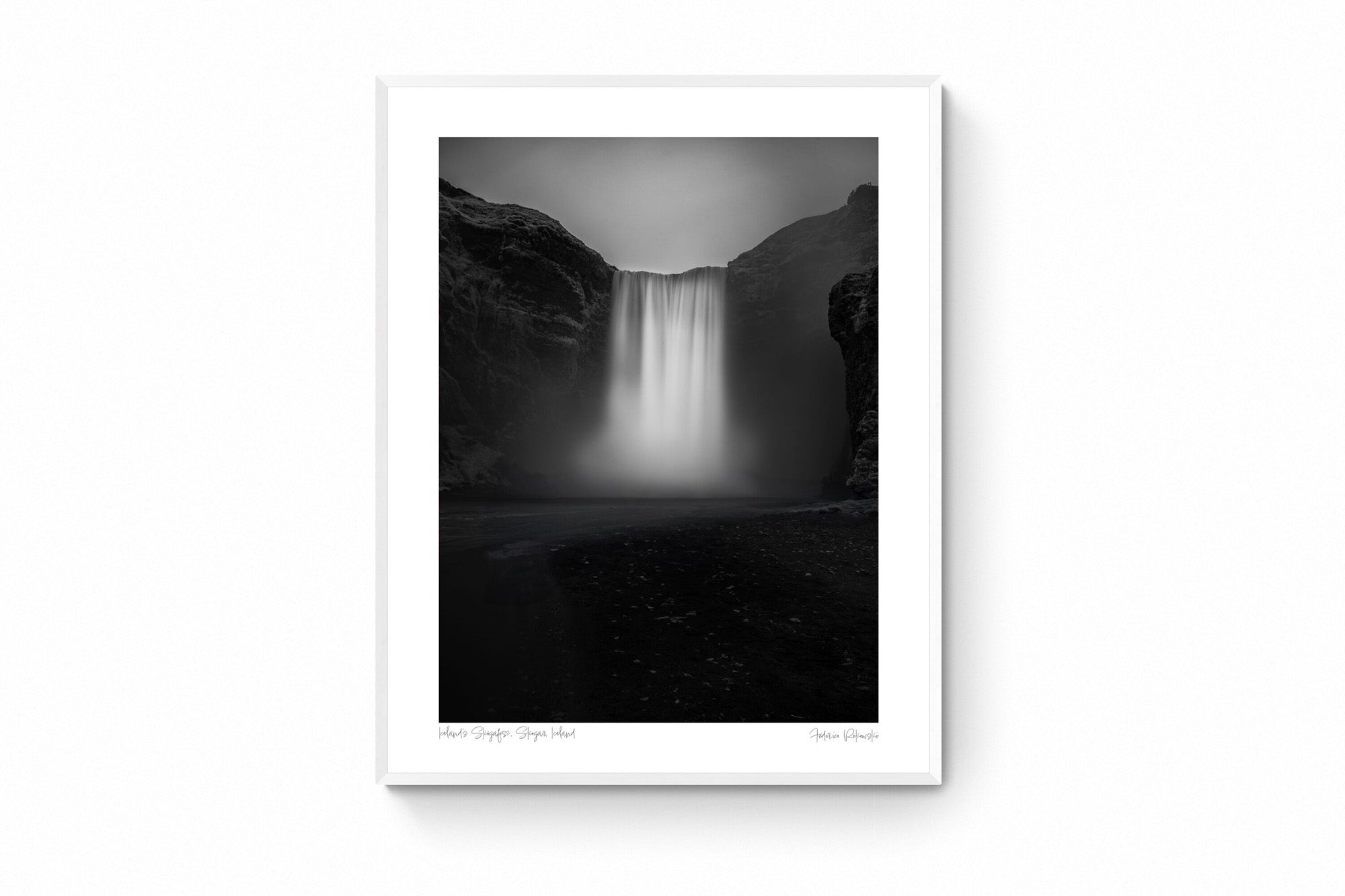 A long exposure photograph of Skógafoss waterfall in Iceland, rendered in stunning black and white, capturing the smooth flow of water between two dark cliffs.