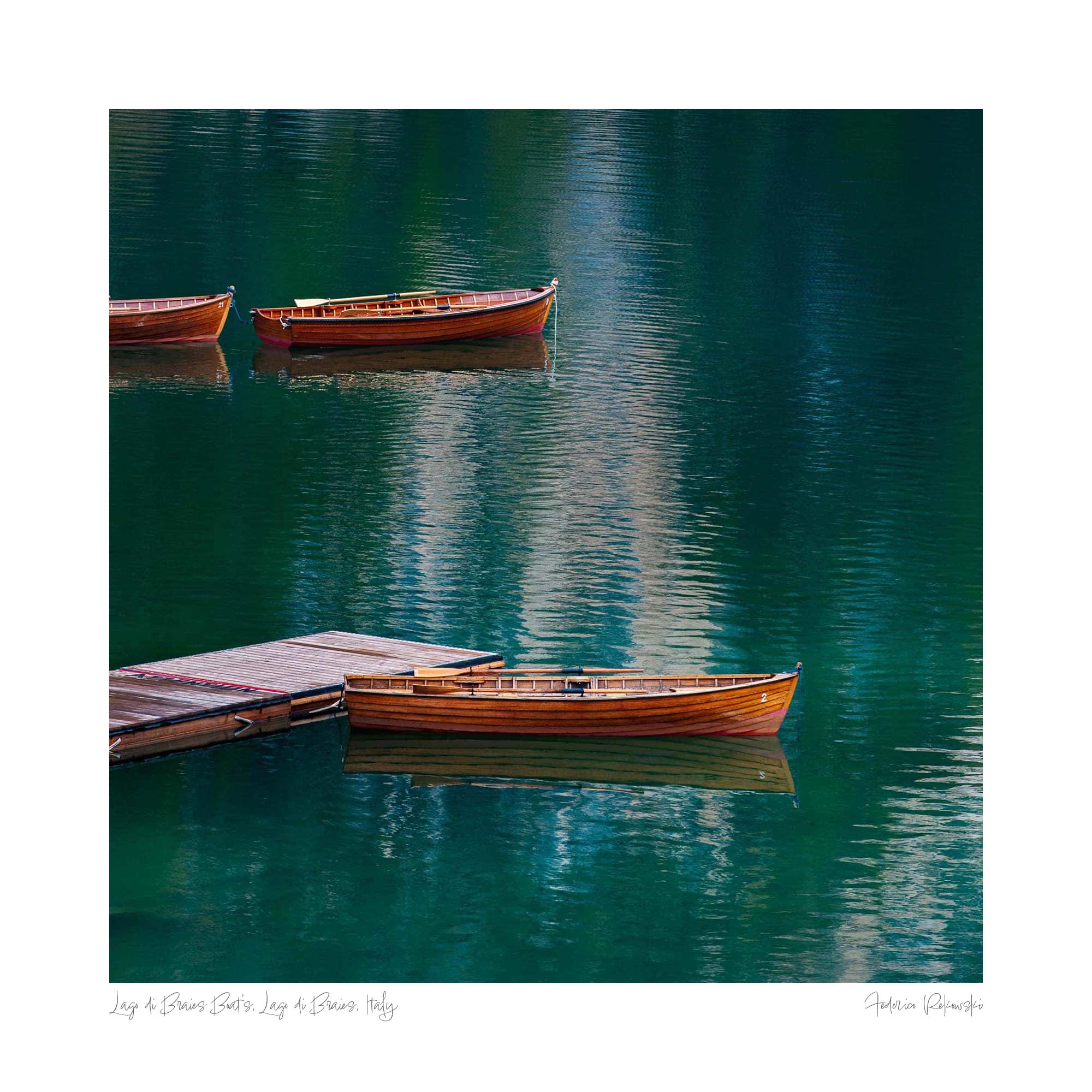 Three wooden boats floating gently on the crystal-clear waters of Lago di Braies in the Dolomites, Italy.