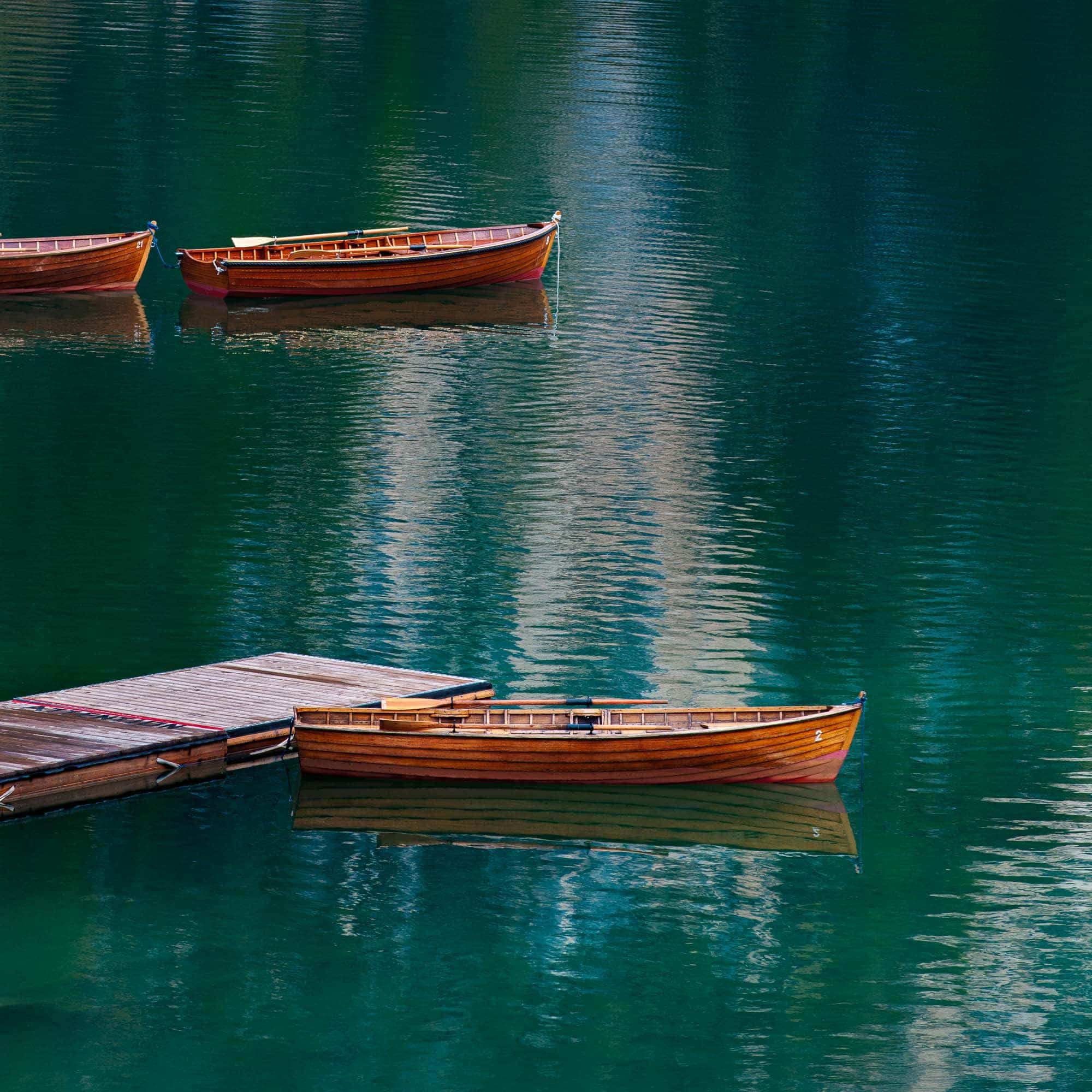 Three wooden boats floating gently on the crystal-clear waters of Lago di Braies in the Dolomites, Italy.