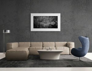 Black and white image of Lago di Braies with still water, reflective boats, a small chapel, and dense trees in the background.