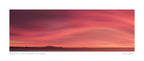 Sunrise over Moeraki Beach depicted in a photograph, showcasing vibrant red and pink clouds stretched across the sky.