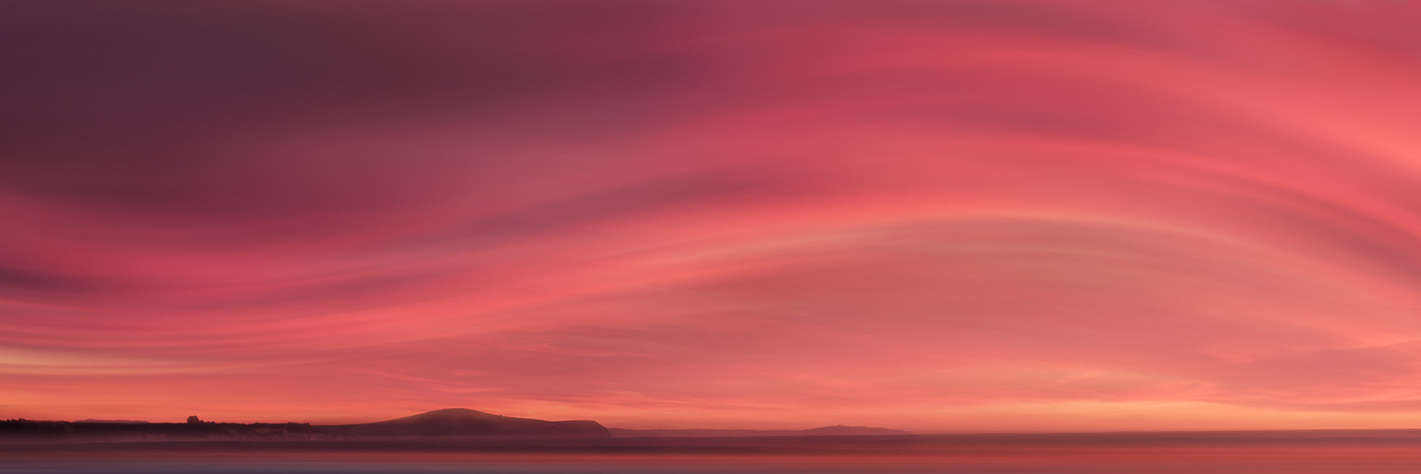 Sunrise over Moeraki Beach depicted in a photograph, showcasing vibrant red and pink clouds stretched across the sky.