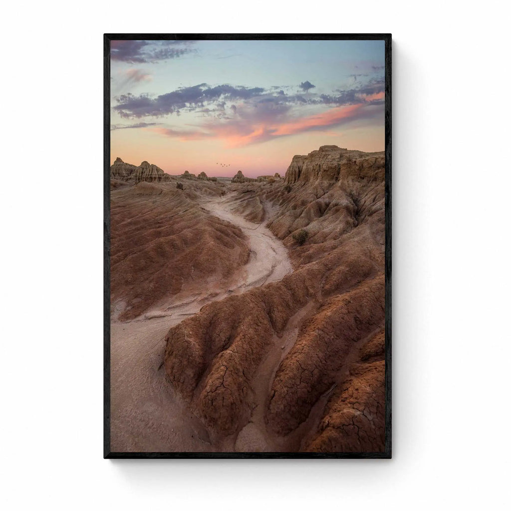 A dusty path through the eroded formations of Mungo National Park, under a sunset sky with streaks of pink and blue. Framed as wall art