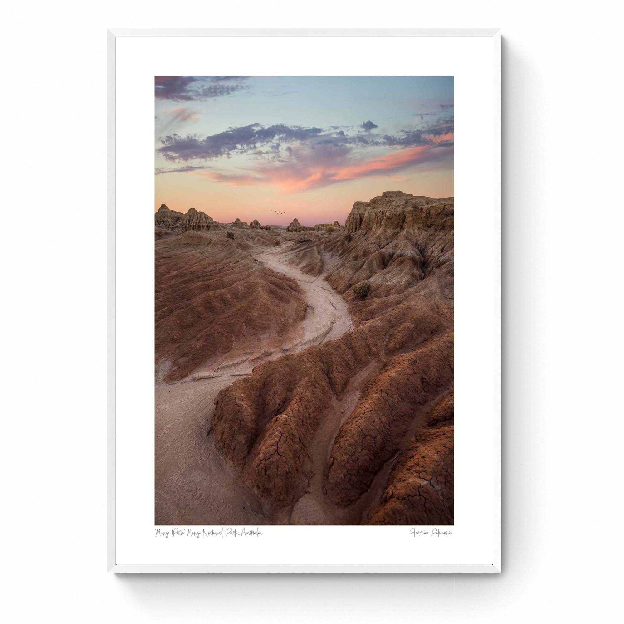 A dusty path through the eroded formations of Mungo National Park, under a sunset sky with streaks of pink and blue. Framed