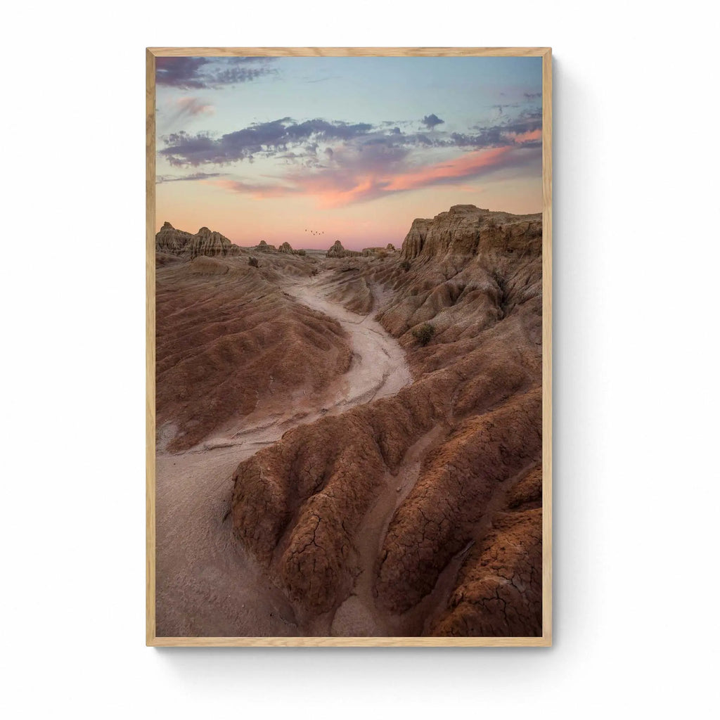 A dusty path through the eroded formations of Mungo National Park, under a sunset sky with streaks of pink and blue. Framed as wall art