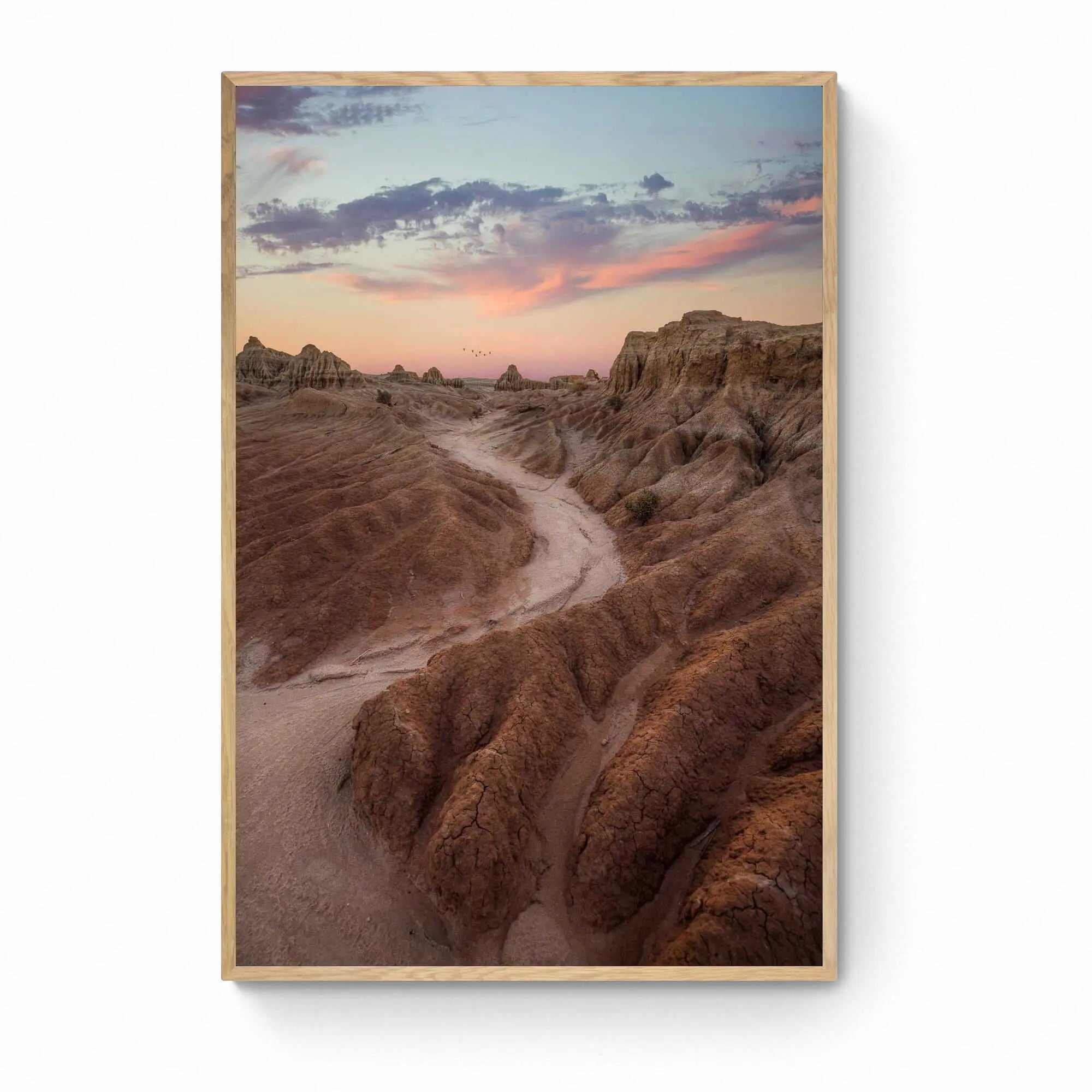 A dusty path through the eroded formations of Mungo National Park, under a sunset sky with streaks of pink and blue. Framed as wall art