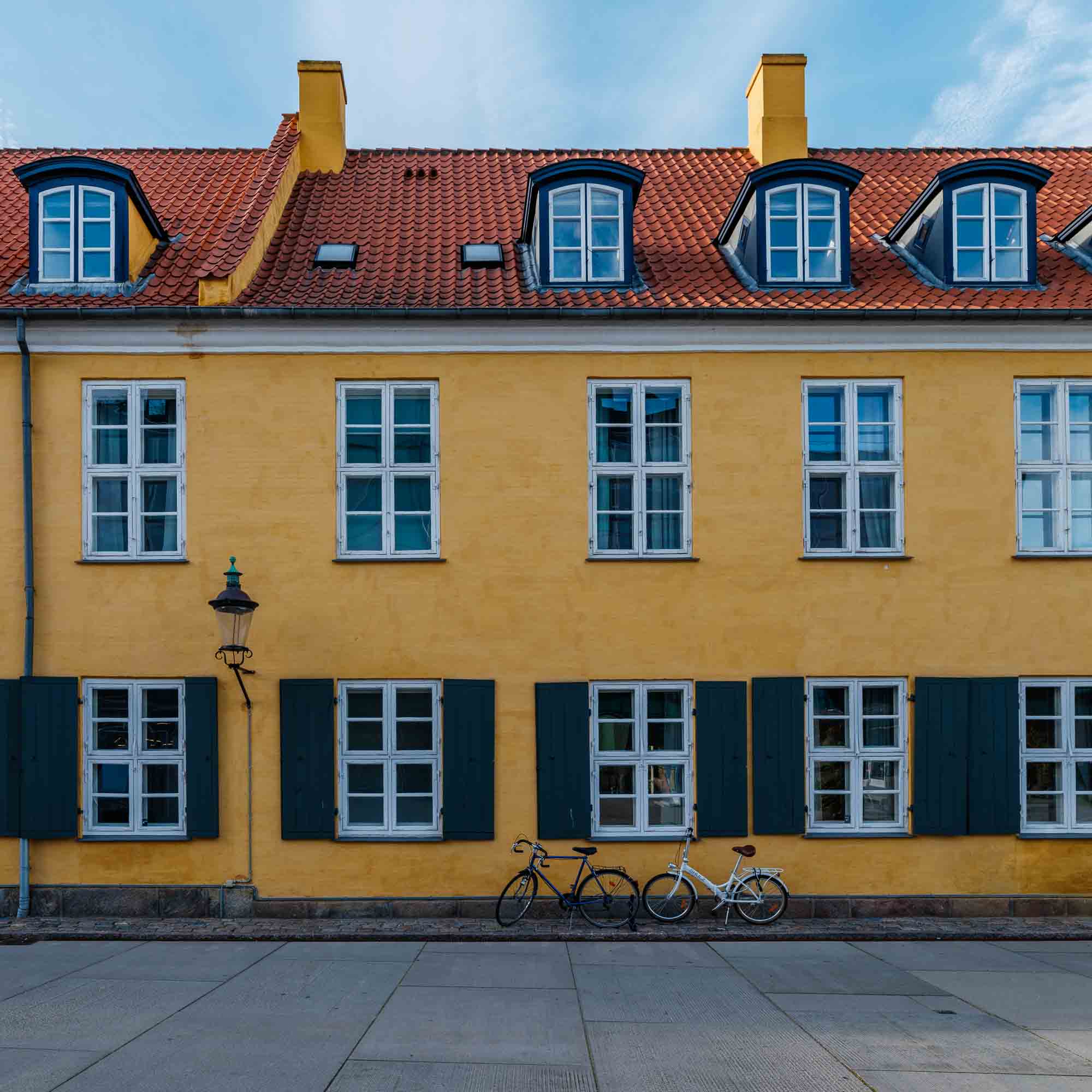 "Colorful image of a yellow building with green shutters and a bicycle in front on a street in Copenhagen, Denmark."