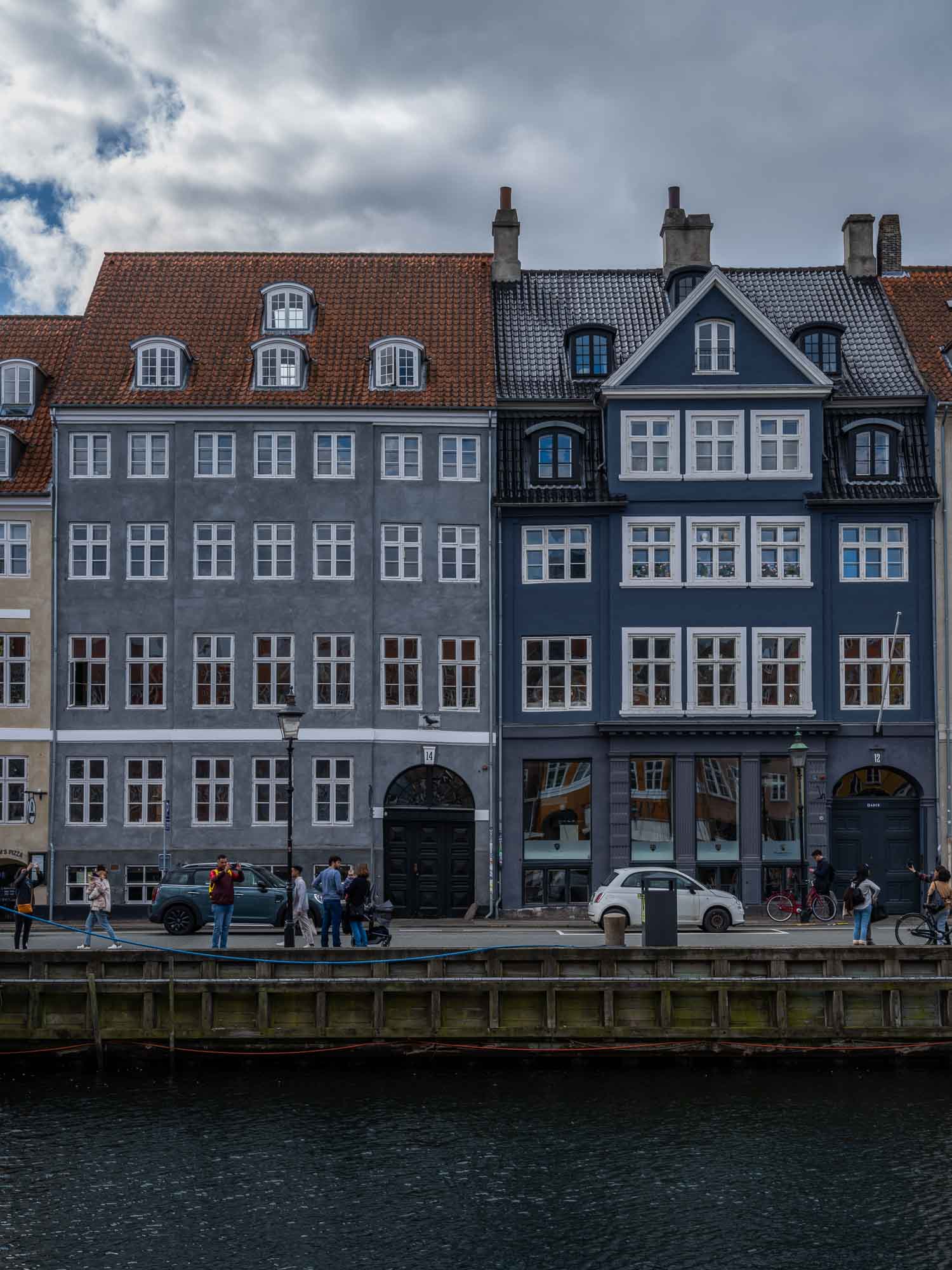 Colorful buildings along the Nyhavn canal in Copenhagen, with people walking and bikes lining the harborside.