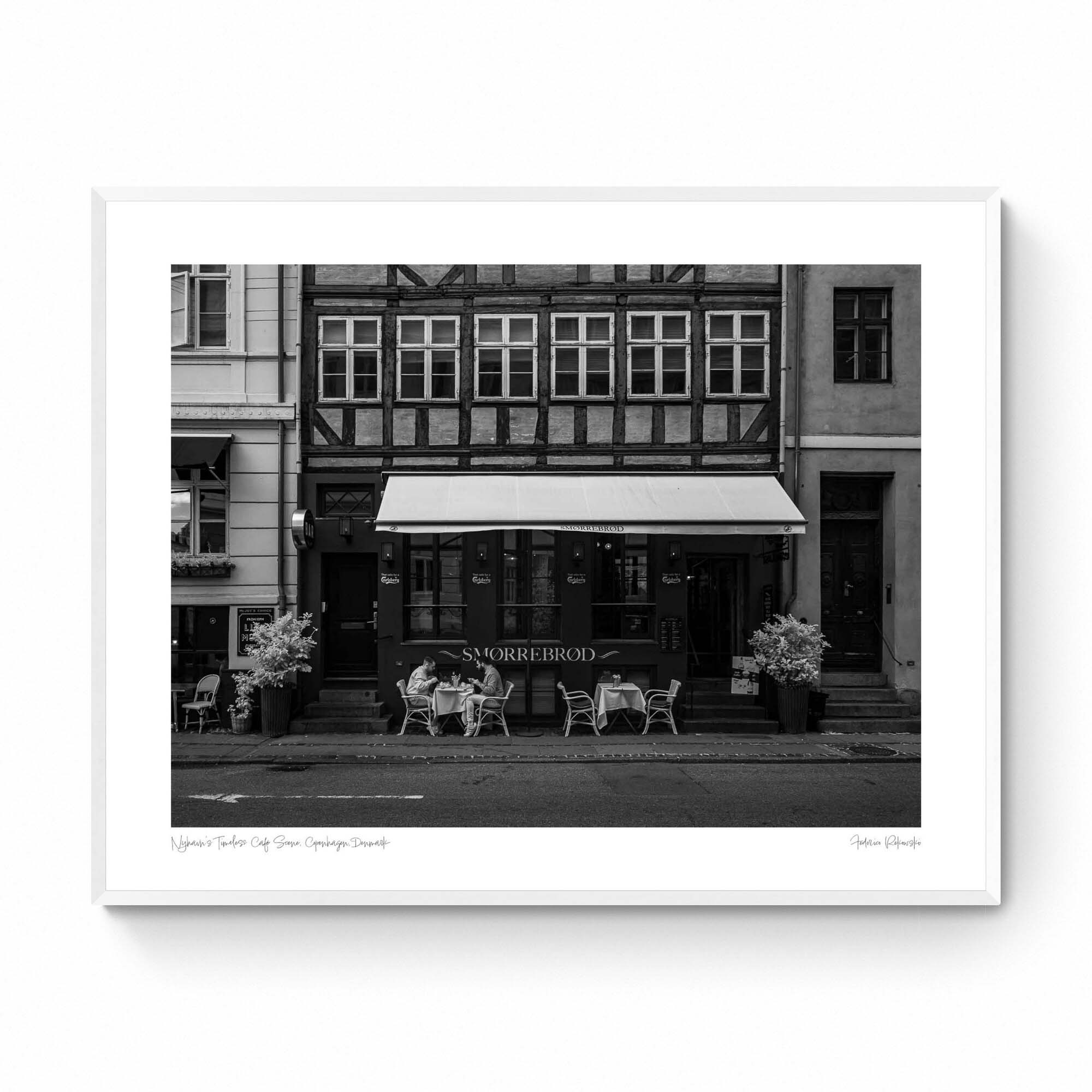 Black and white photo of a traditional Danish Smørrebrød café in Nyhavn, Copenhagen, with outdoor seating and historical buildings.