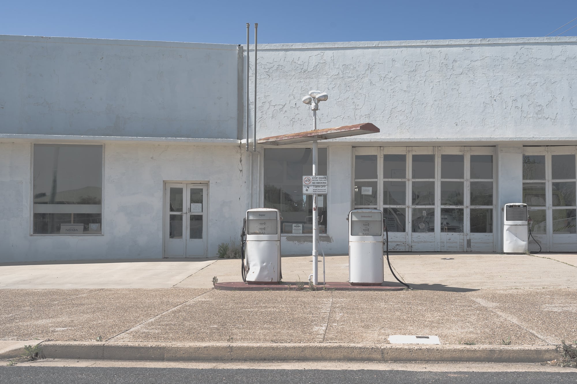A desolate scene of an abandoned fuel station with obsolete pumps in Cowra, NSW, under a broad daylight sky.