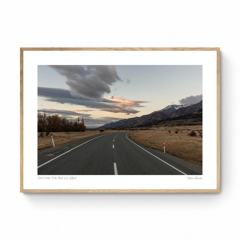 A serene landscape photograph of a road in New Zealand with Aoraki/Mt Cook in the background under a twilight sky with dynamic cloud formations.